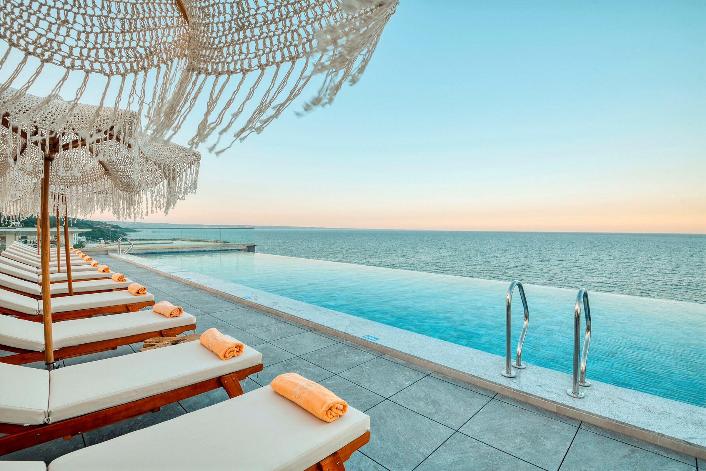 Liggestole med orange håndklæder ved en infinity-pool med udsigt over havet. (AI-genereret tekst)