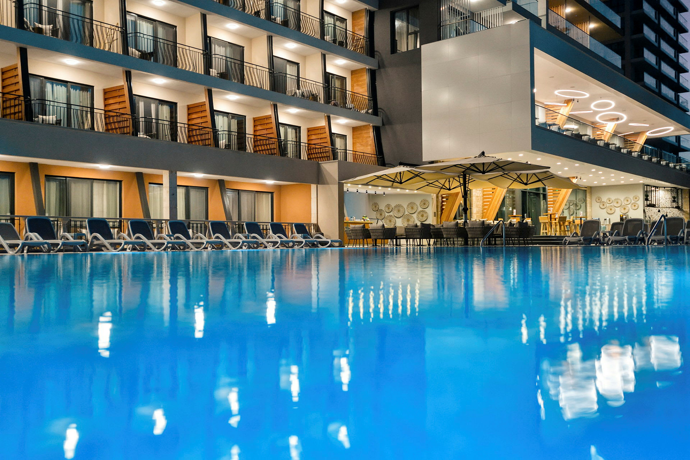Et hotel med en udendørs pool, omgivet af liggestole og en restaurant med tag og borddækning. (AI-genereret tekst)