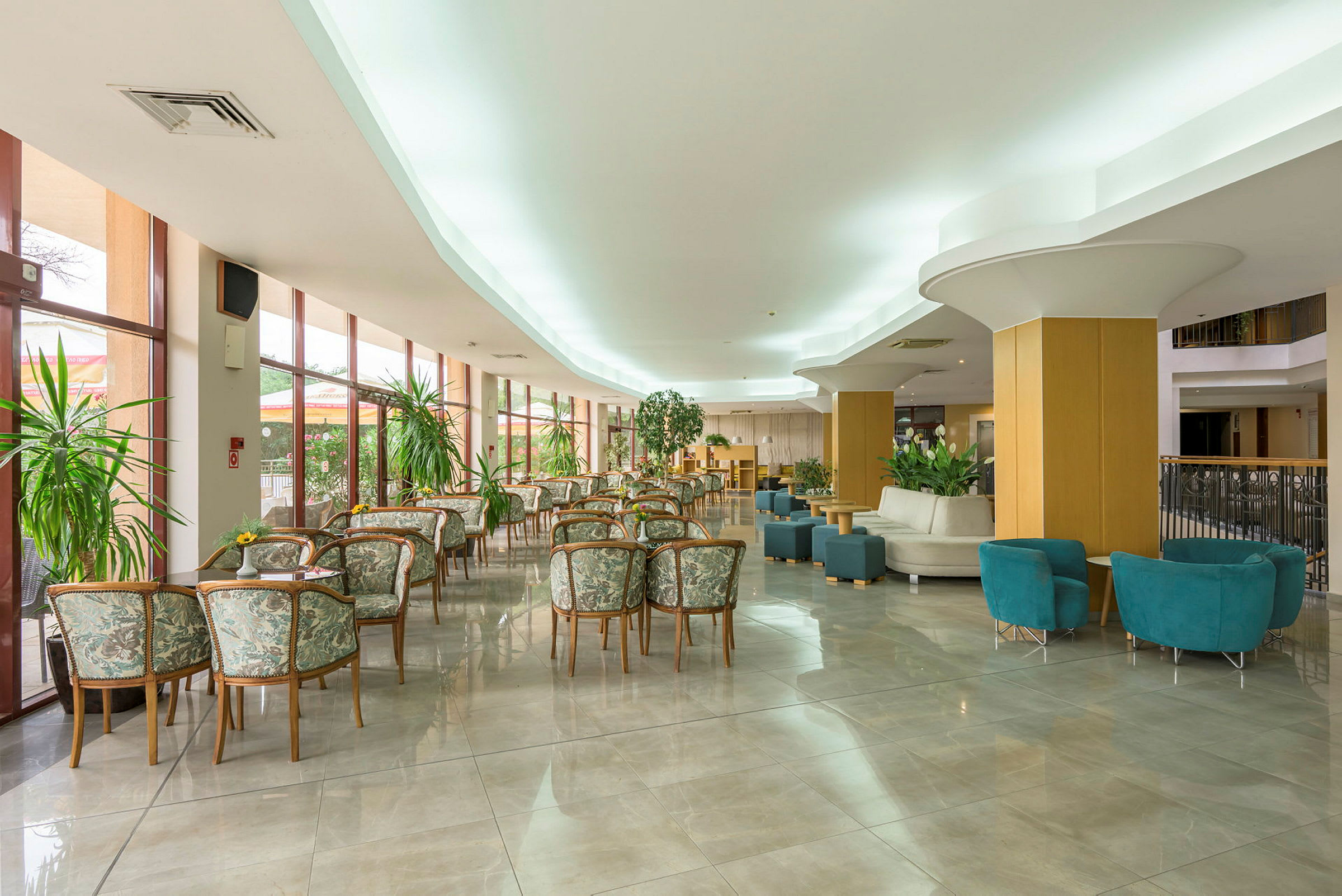 Hotellobby med borde og stole samt grønne planter. (AI-genereret tekst)