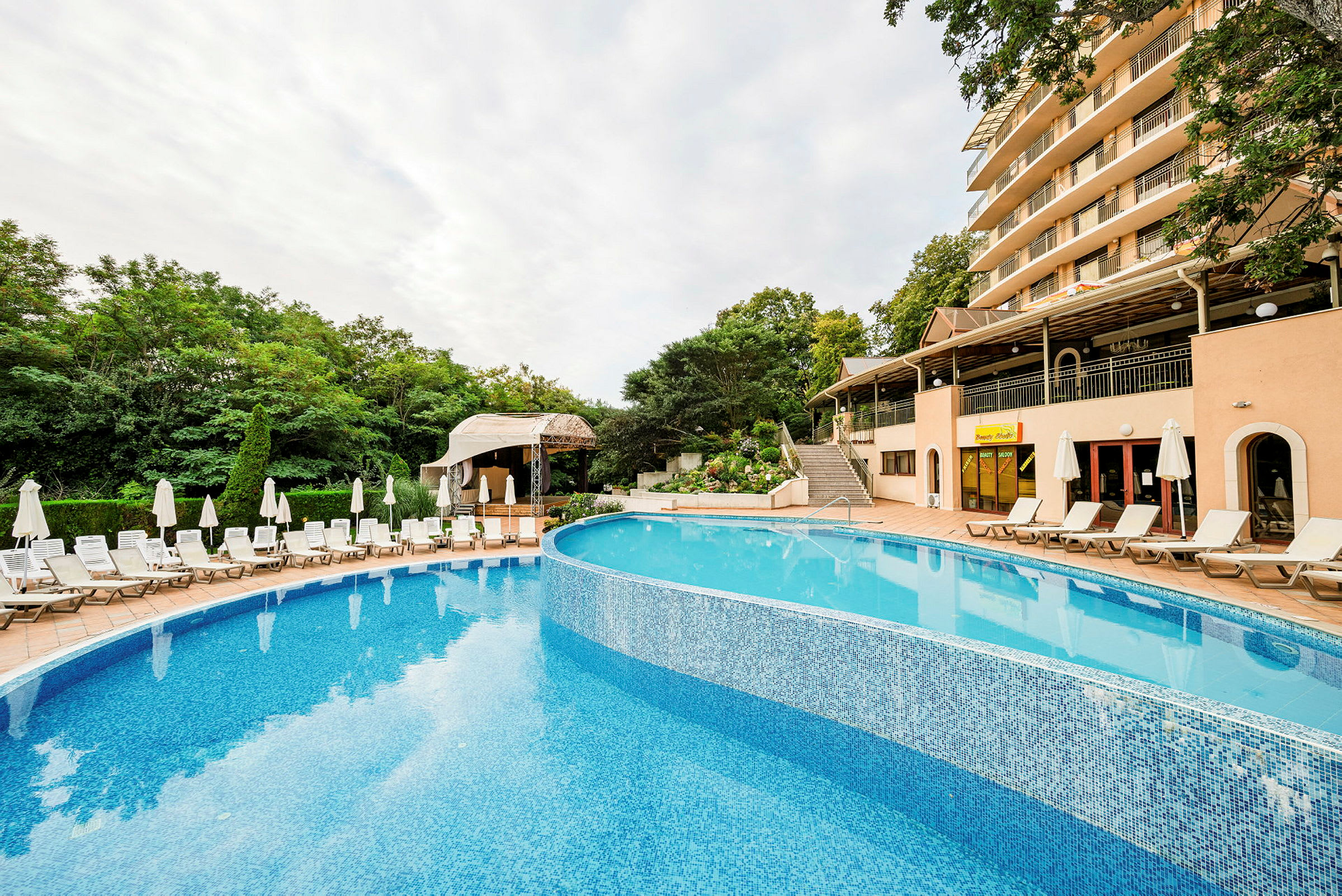 Udendørsområde med en pool, solsenge og et hotel i baggrunden. (AI-genereret tekst)
