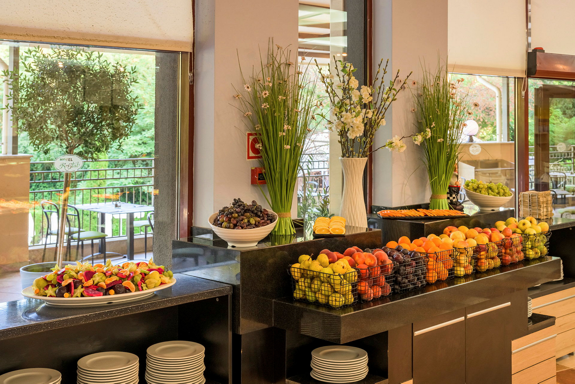 Billede af en buffet med frisk frugt og dekorationer samt udsigt til en terrasse. (AI-genereret tekst)