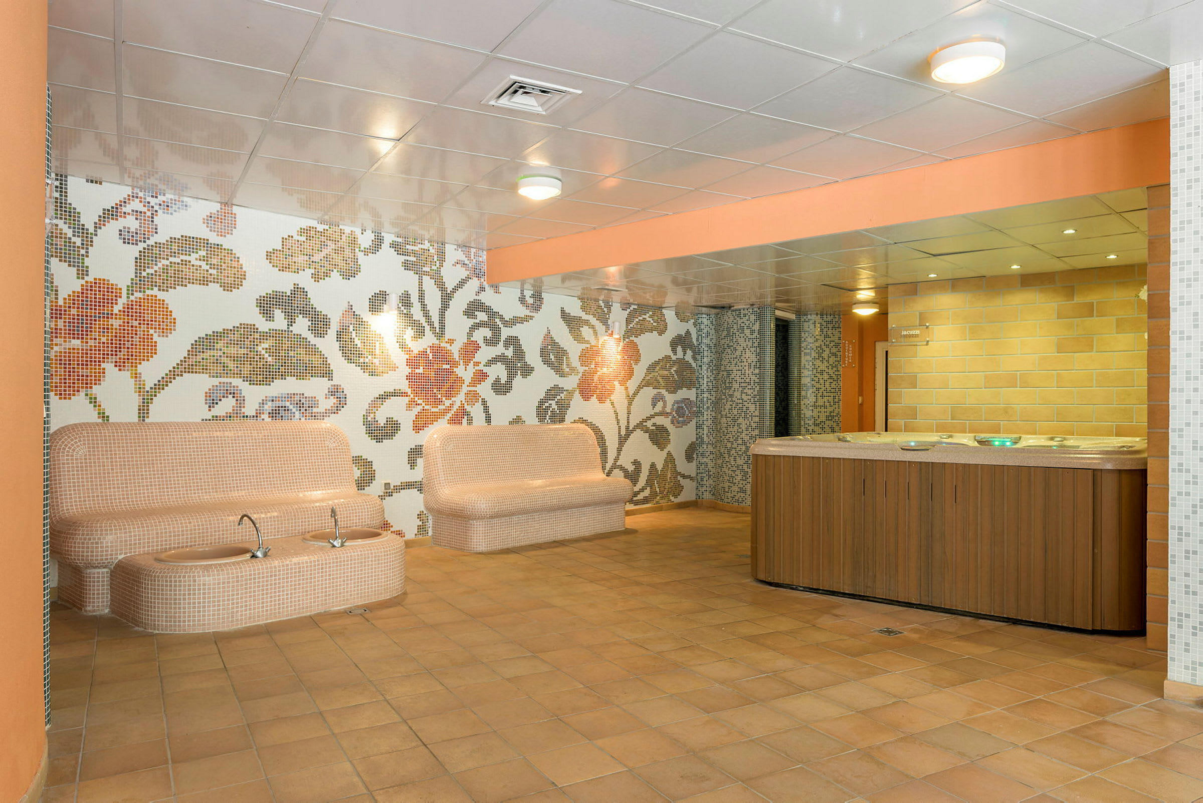 Interiør af et spaområde med siddepladser, detaljeret mønster på væggene og en jacuzzi. (AI-genereret tekst)