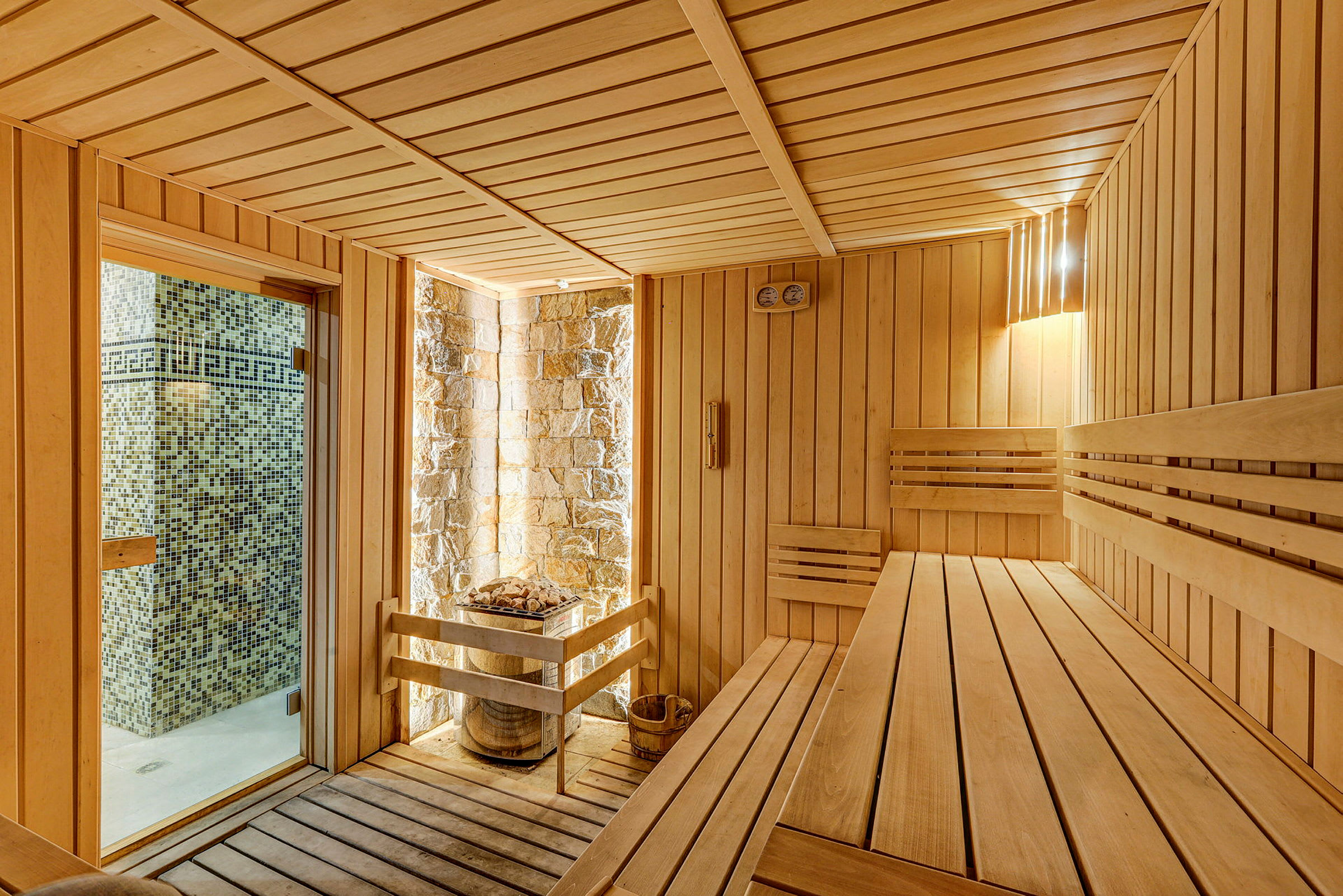En rummelig sauna med træpaneler og siddebænke, med et vindue der viser en flisebelagt væg udenfor. (AI-genereret tekst)