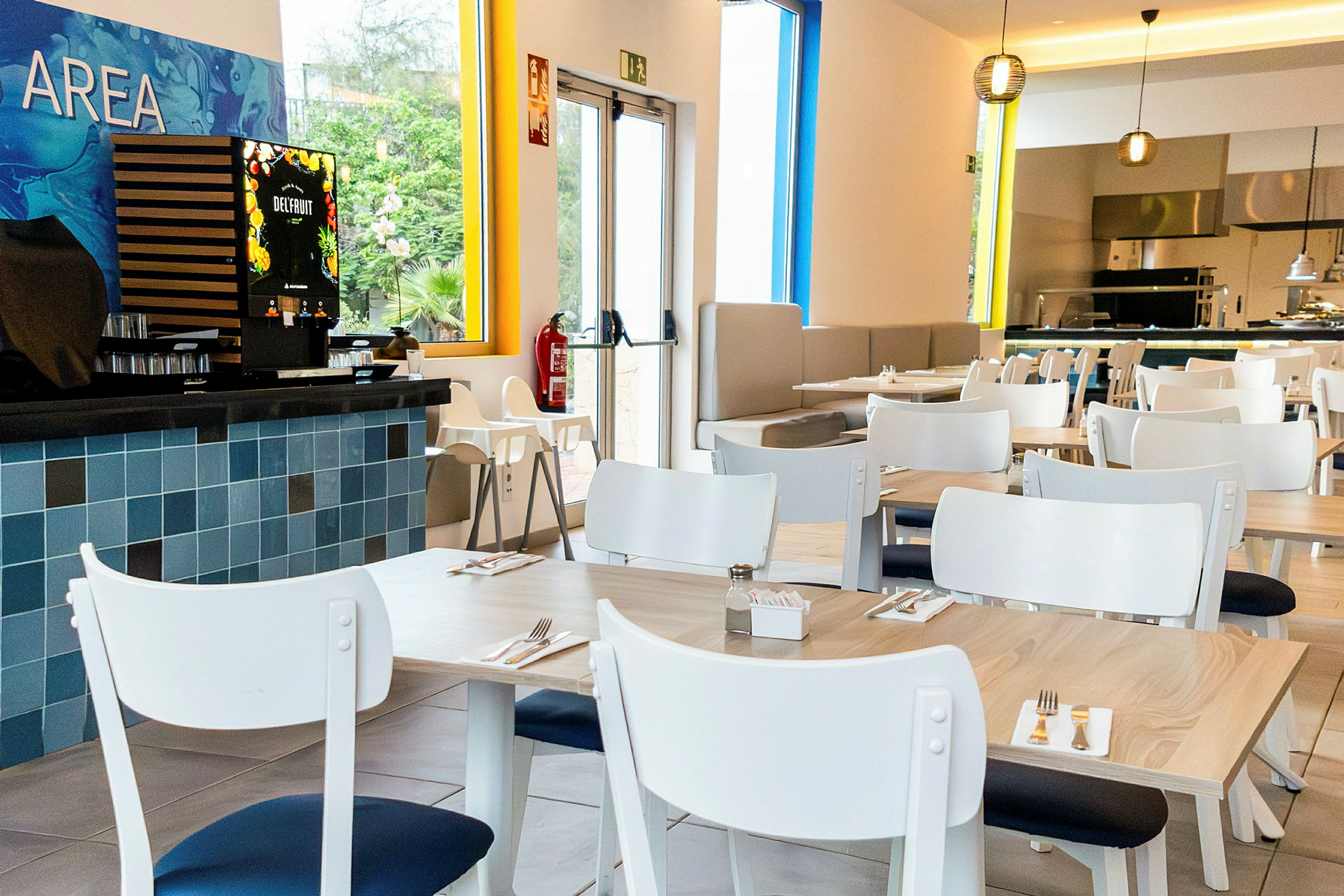 En moderne restaurant med hvide borde og stole. En juiceautomat kan ses til venstre. (AI-genereret tekst)