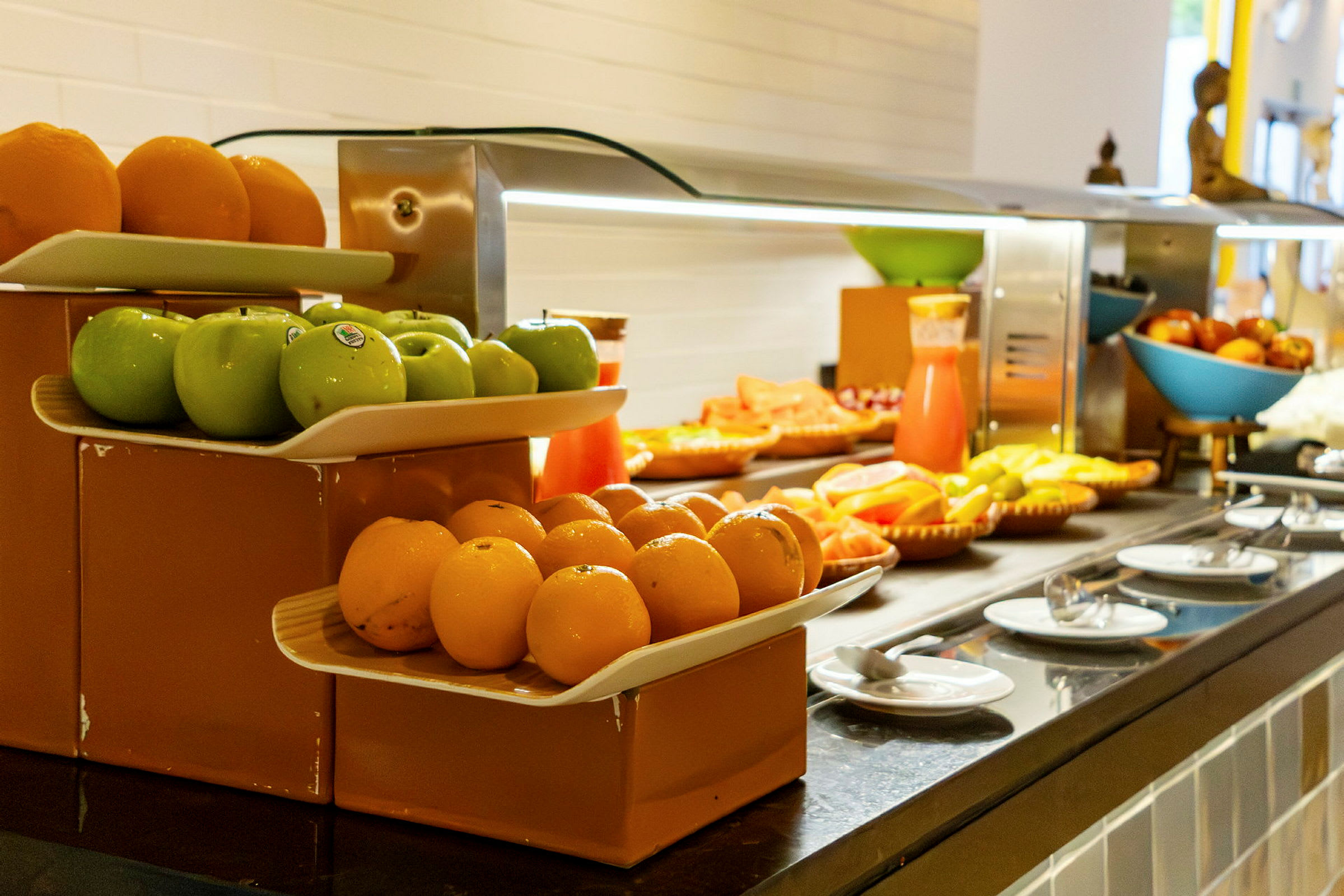 Frugtbuffet med grønne æbler, appelsiner og andet frugt samt en saftkande. (AI-genereret tekst)