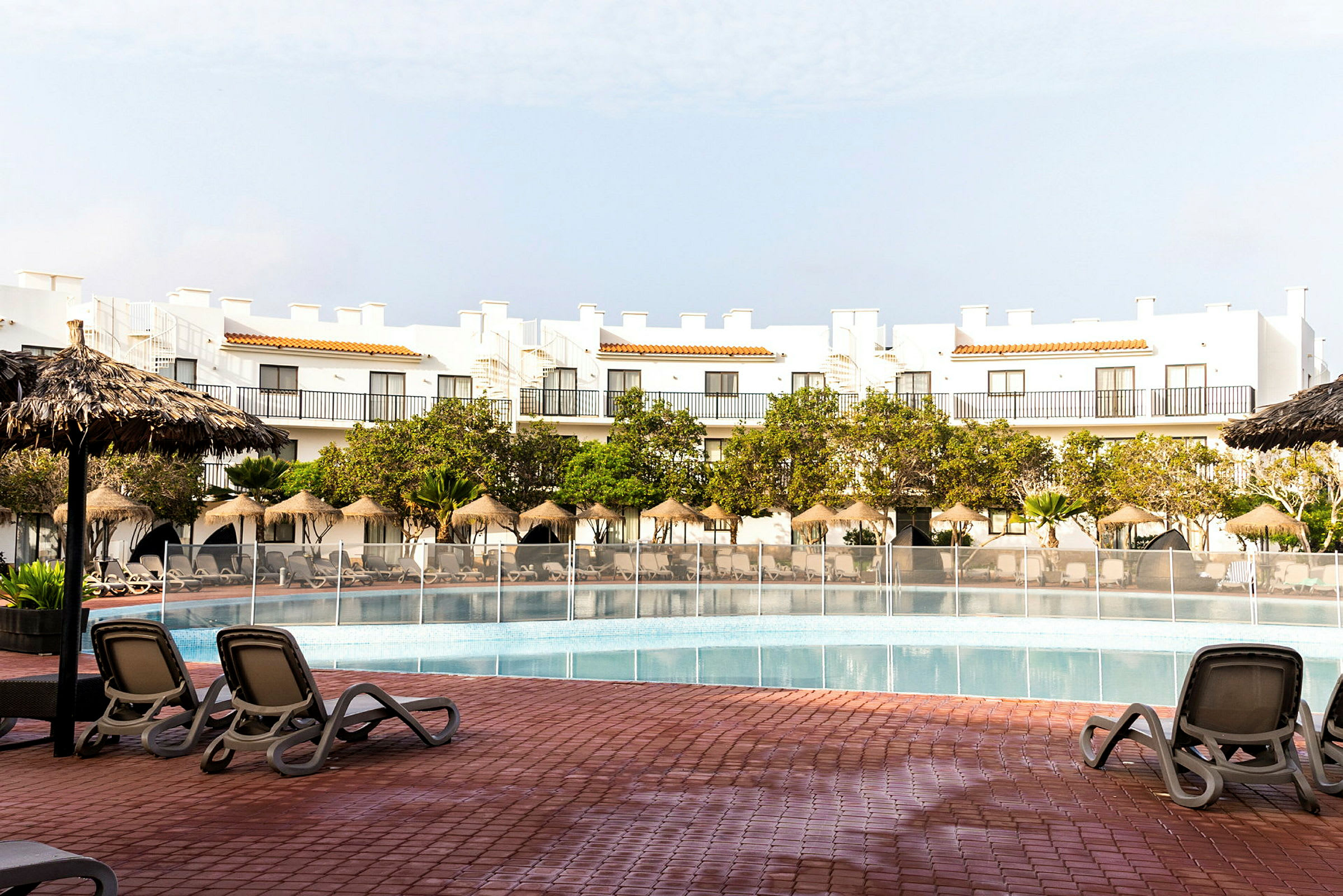 Udendørs swimmingpool med liggestole, parasoller og hotelbygning i baggrunden. (AI-genereret tekst)