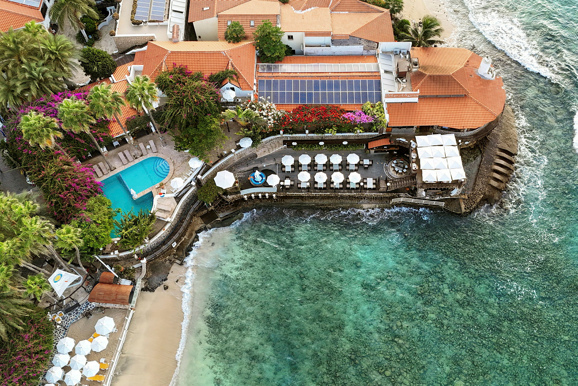 Luftfoto af en bygning ved havet med pool og udendørsområder. (AI-genereret tekst)