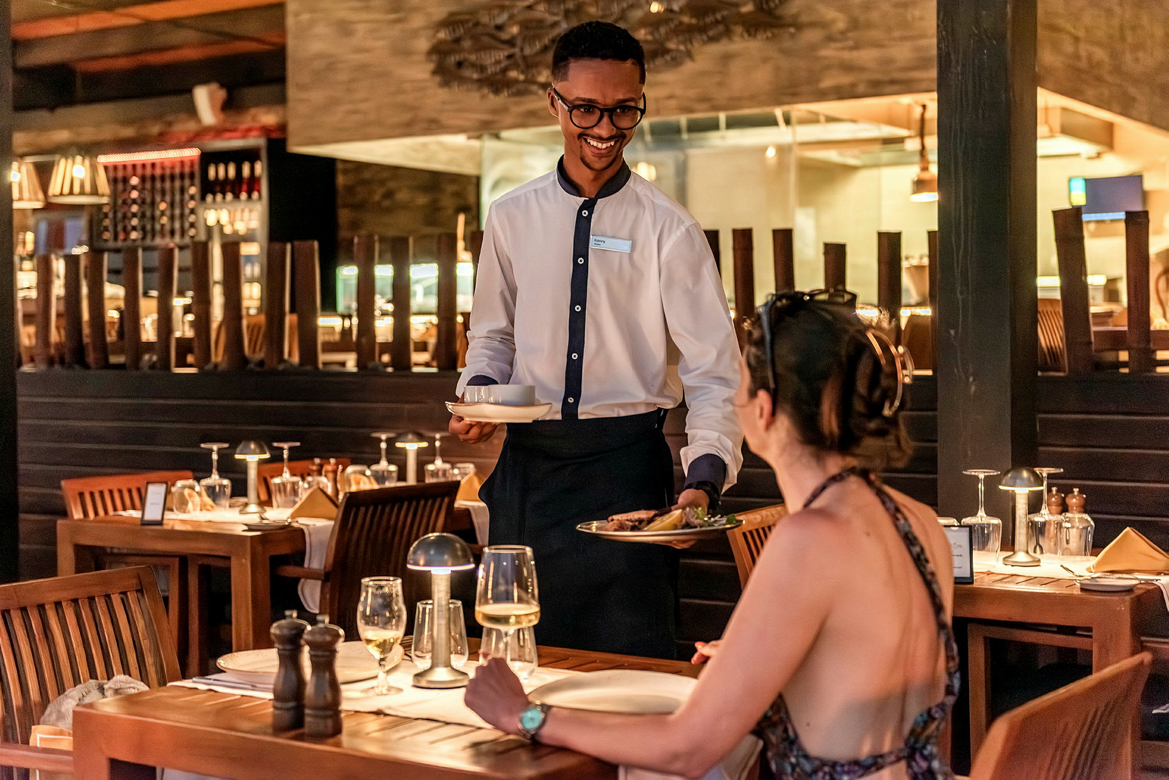 En tjener serverer mad til en kvinde ved et restaurantbord. (AI-genereret tekst)