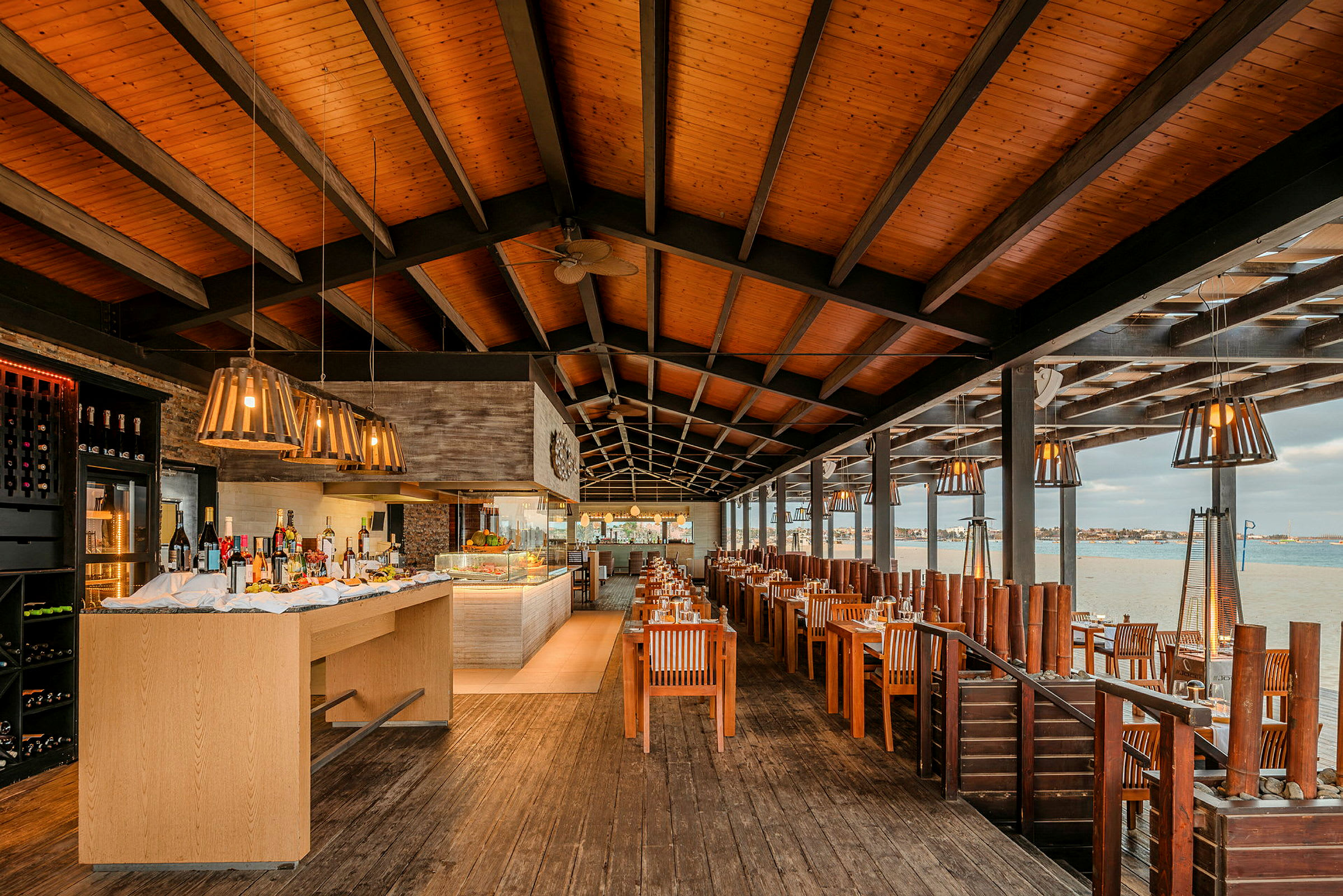 Restaurant ved vandet med dækkede borde, træinteriør og loftsdekorationer. (AI-genereret tekst)