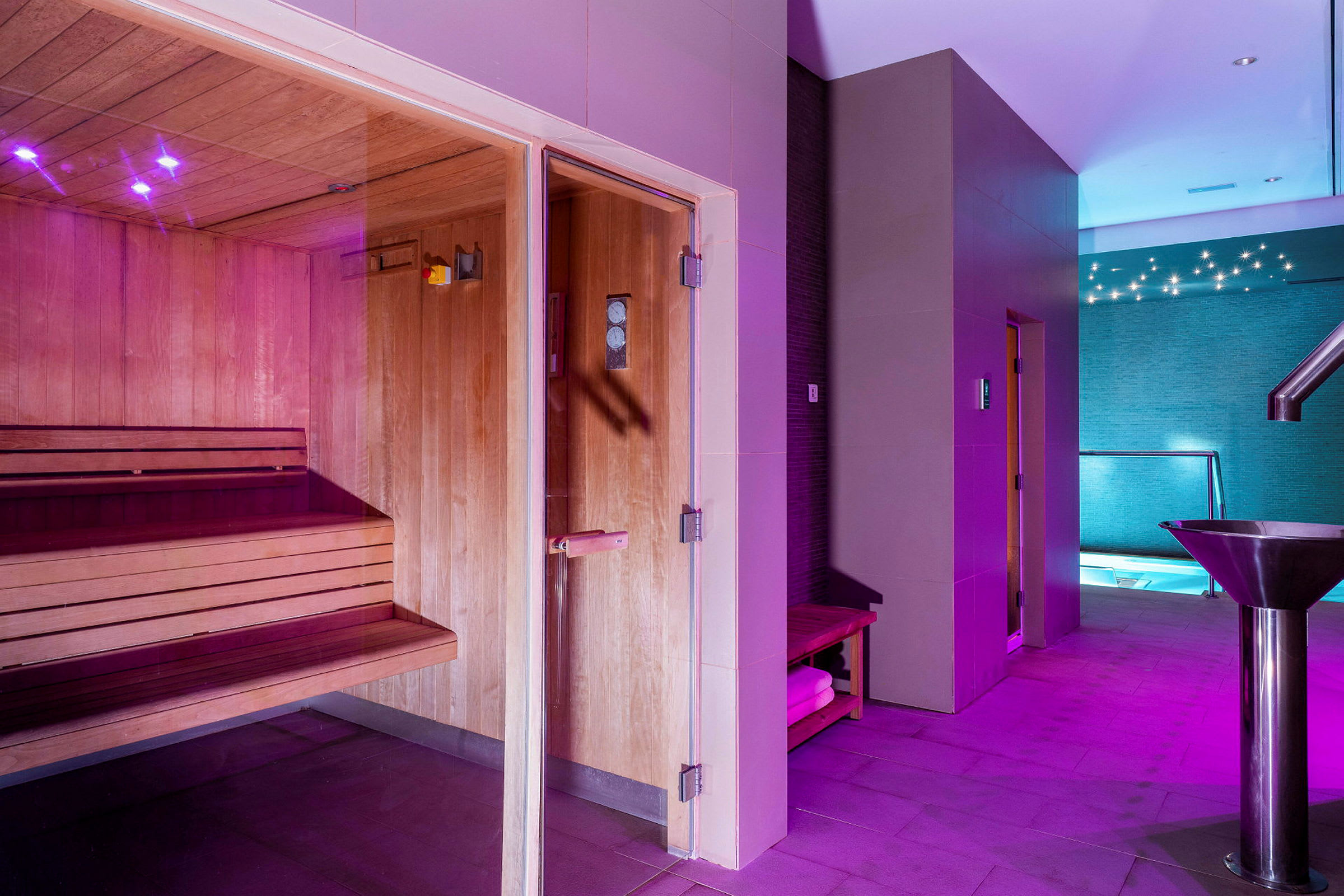 Et spa der viser en sauna med træpaneler, en gang med belysning og udsigt til en pool. (AI-genereret tekst)