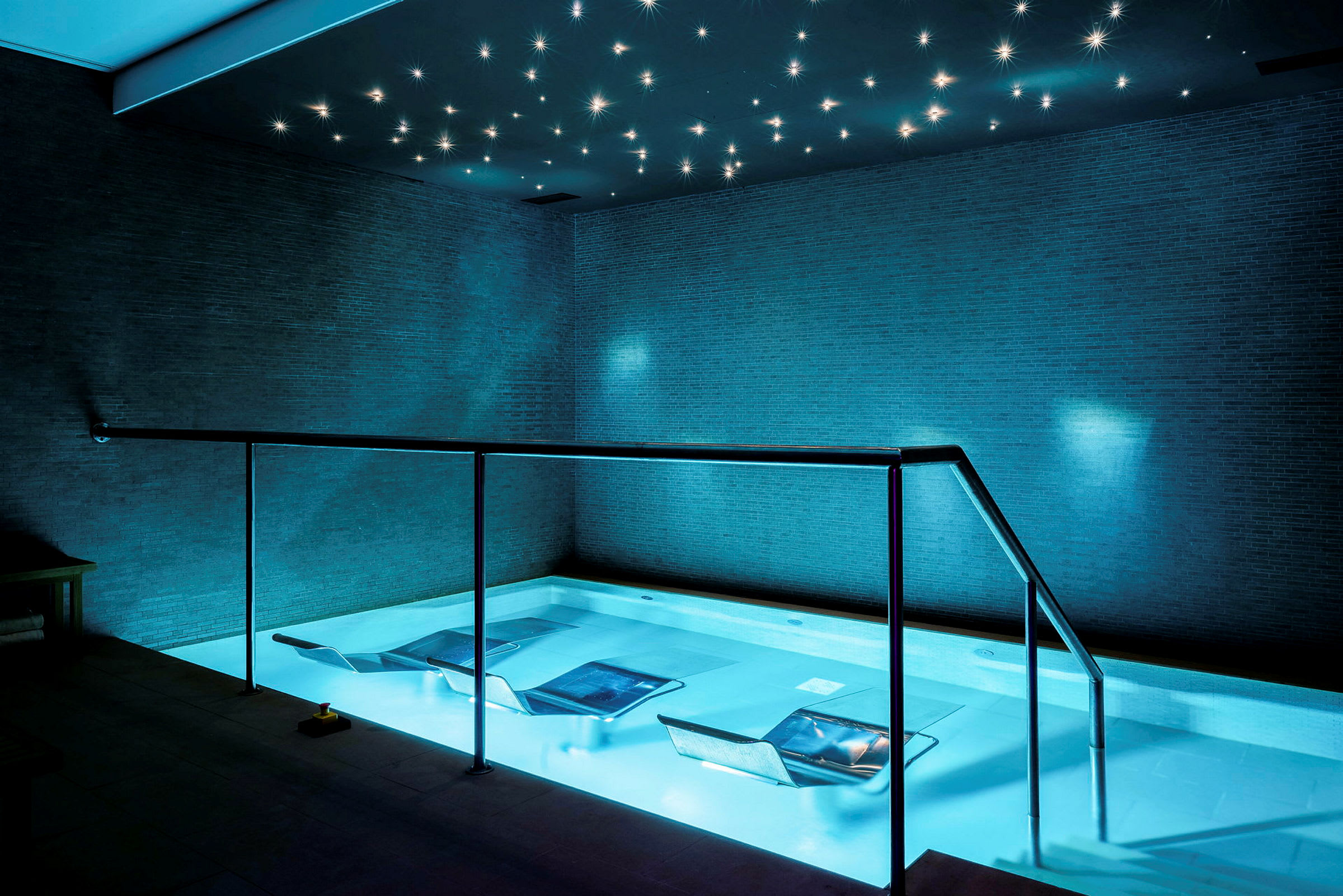 En pool i et spa med afslapningsstole i vandet og en stjerneformet lysinstallation i loftet. (AI-genereret tekst)