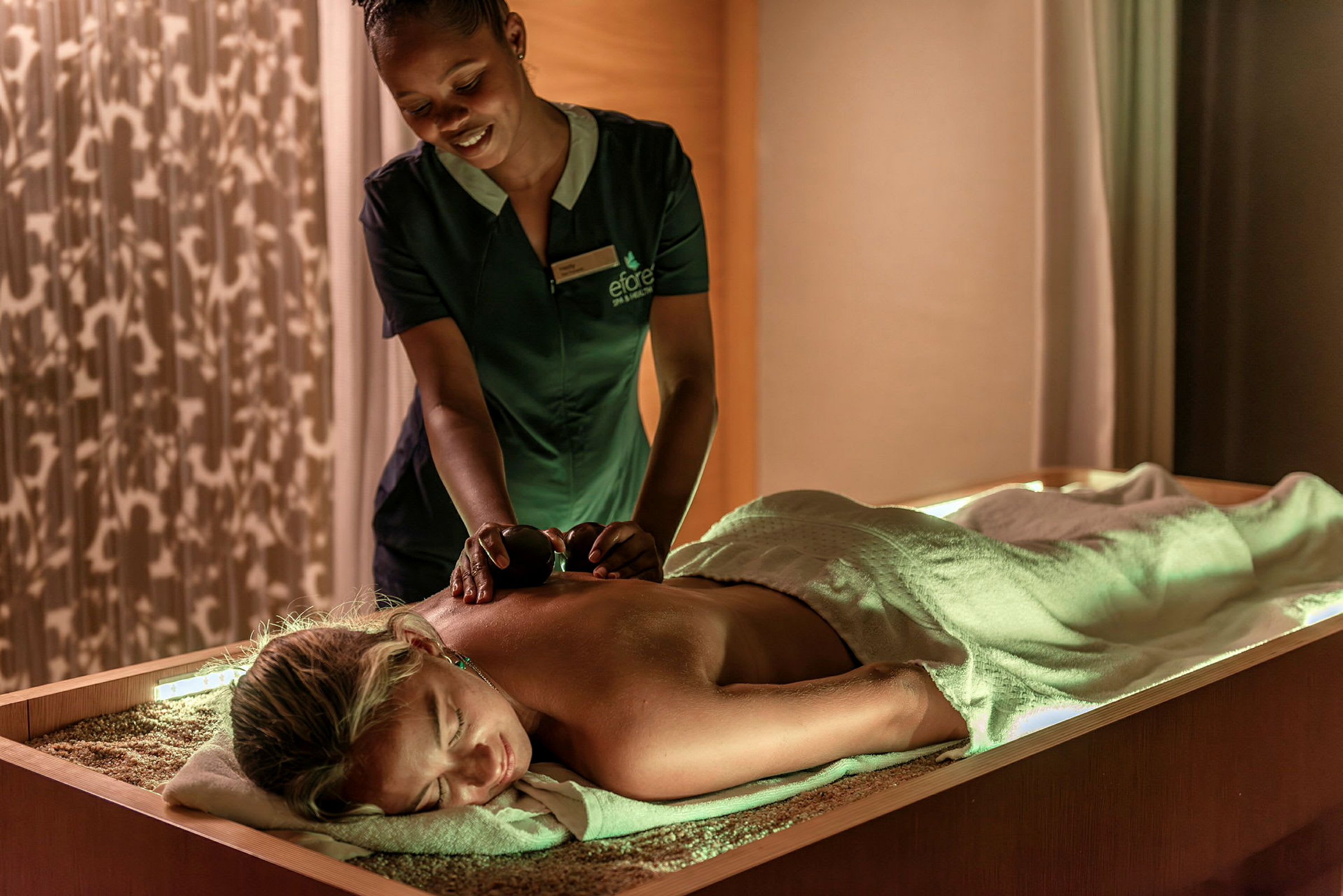 En person modtager en massagebehandling af en massør, der bruger varme sten i et afslappende rum. (AI-genereret tekst)