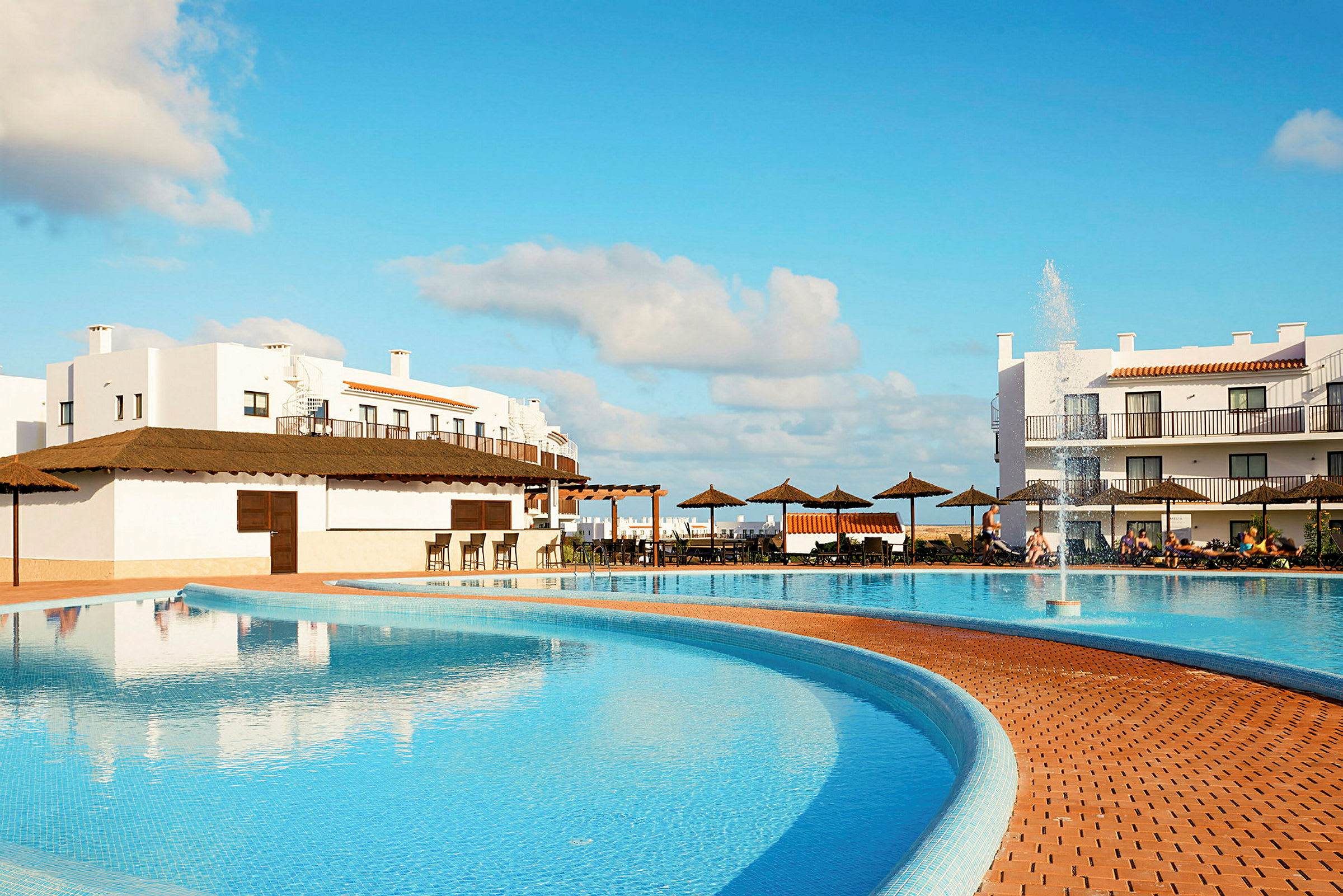 Udendørs pool ved hotel med liggestole og bygninger i baggrunden. (AI-genereret tekst)