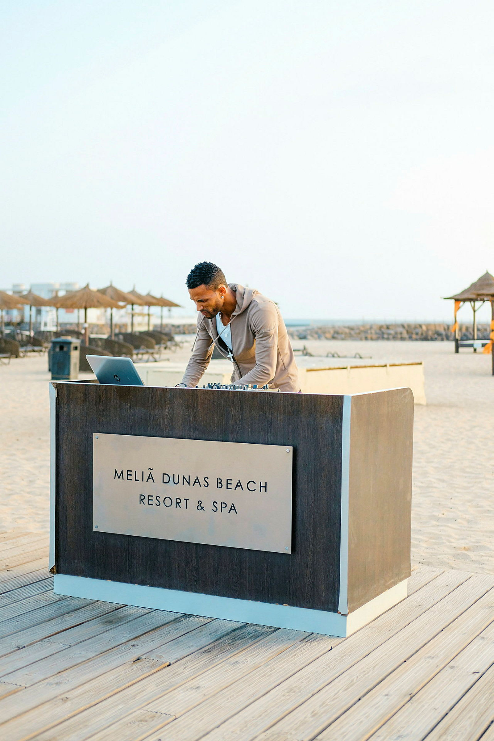 En person står ved et bord med teksten 'Meliã Dunas Beach Resort & Spa' ved stranden. (AI-genereret tekst)