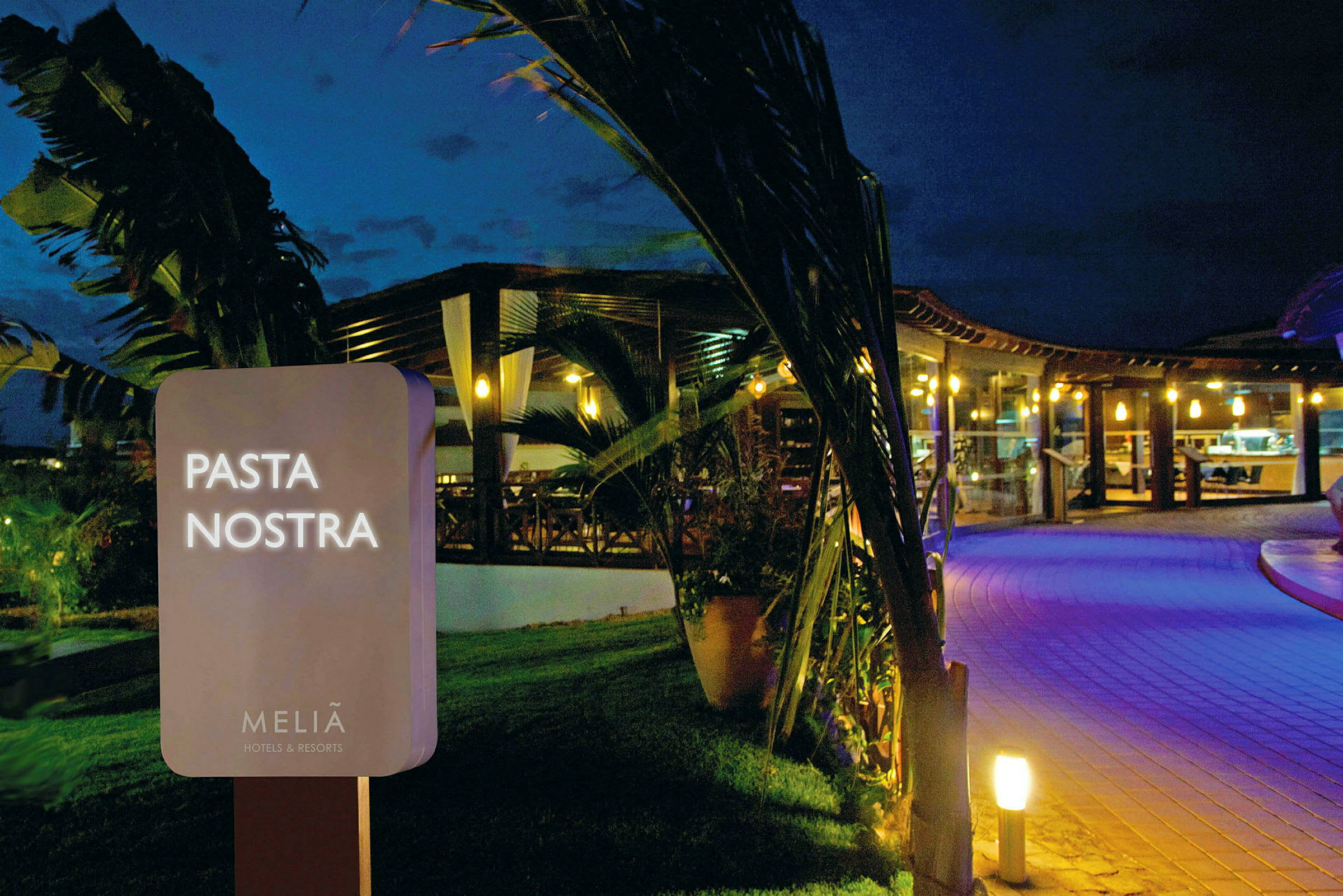 Skilt med teksten 'Pasta Nostra' foran en oplyst restaurant om aftenen. (AI-genereret tekst)