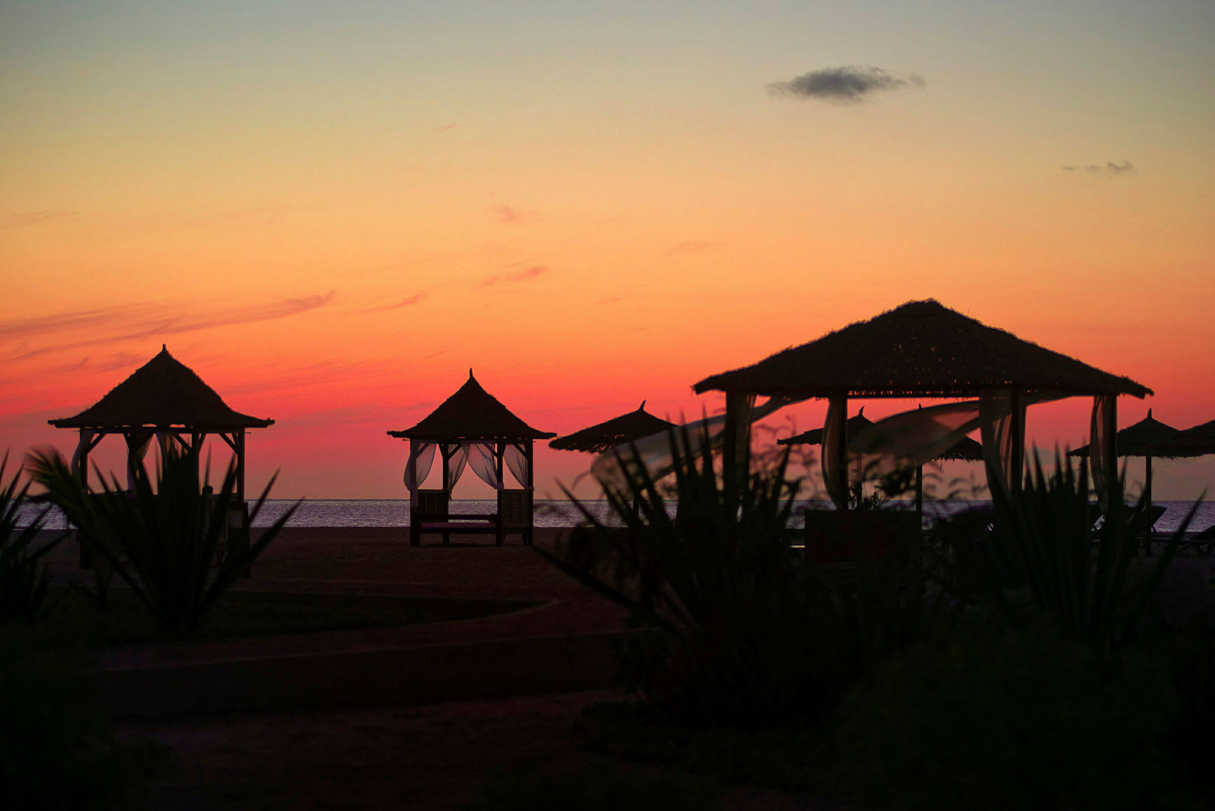 Billede af en strand med solnedgang, hvor flere strandhytter ses i forgrunden. (AI-genereret tekst)