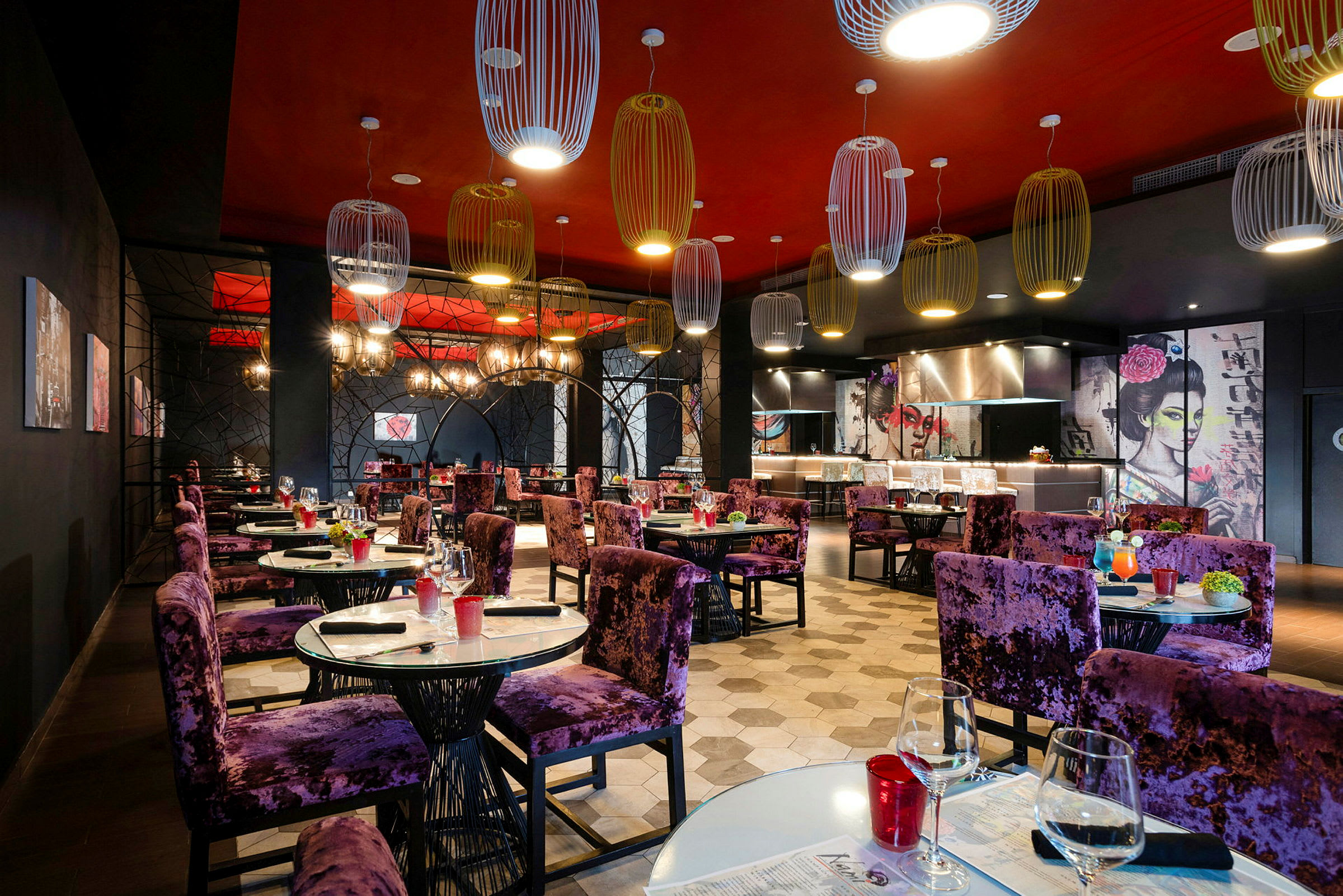 En restaurant med elegant indretning og lilla stole ved dækkede borde. Væggene har kunstneriske motiver, og loftet er dekoreret med moderne lamper. (AI-genereret tekst)
