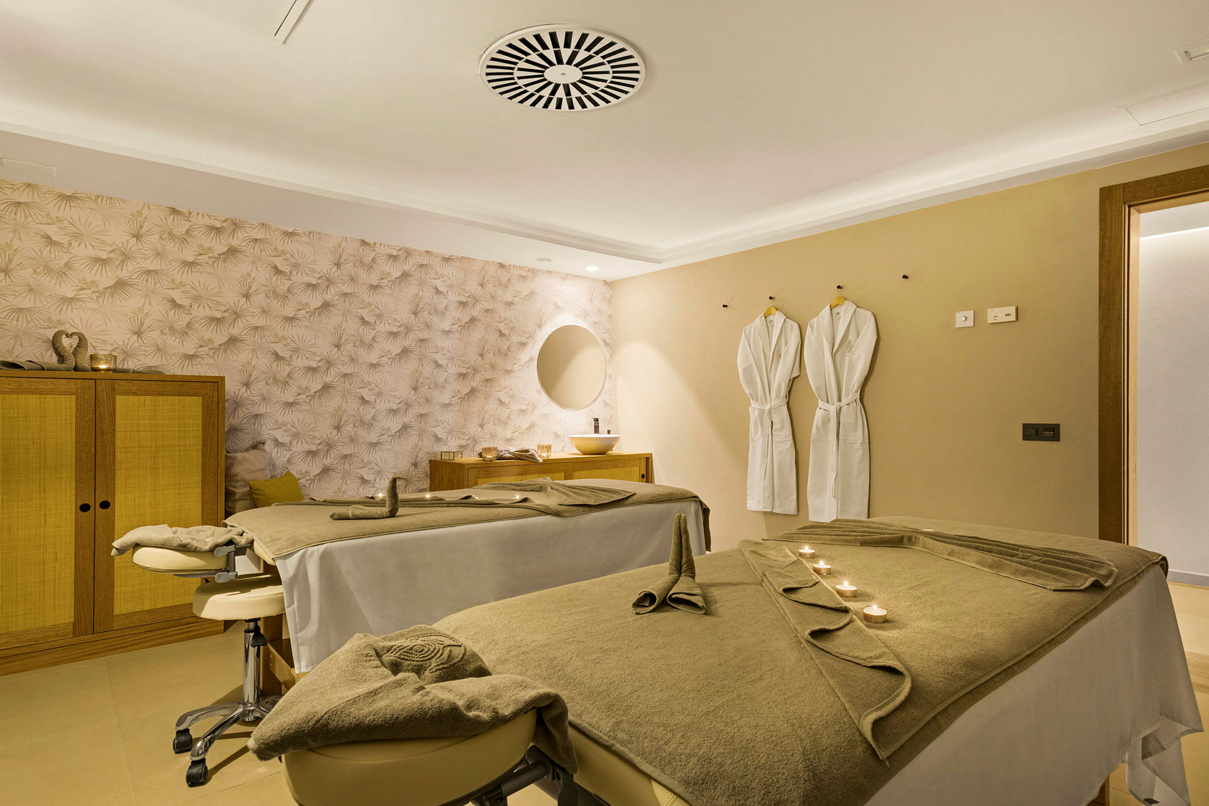 Et spa-rum med to massageborde, to badekåber på væggen og en dekorativ væg. (AI-genereret tekst)