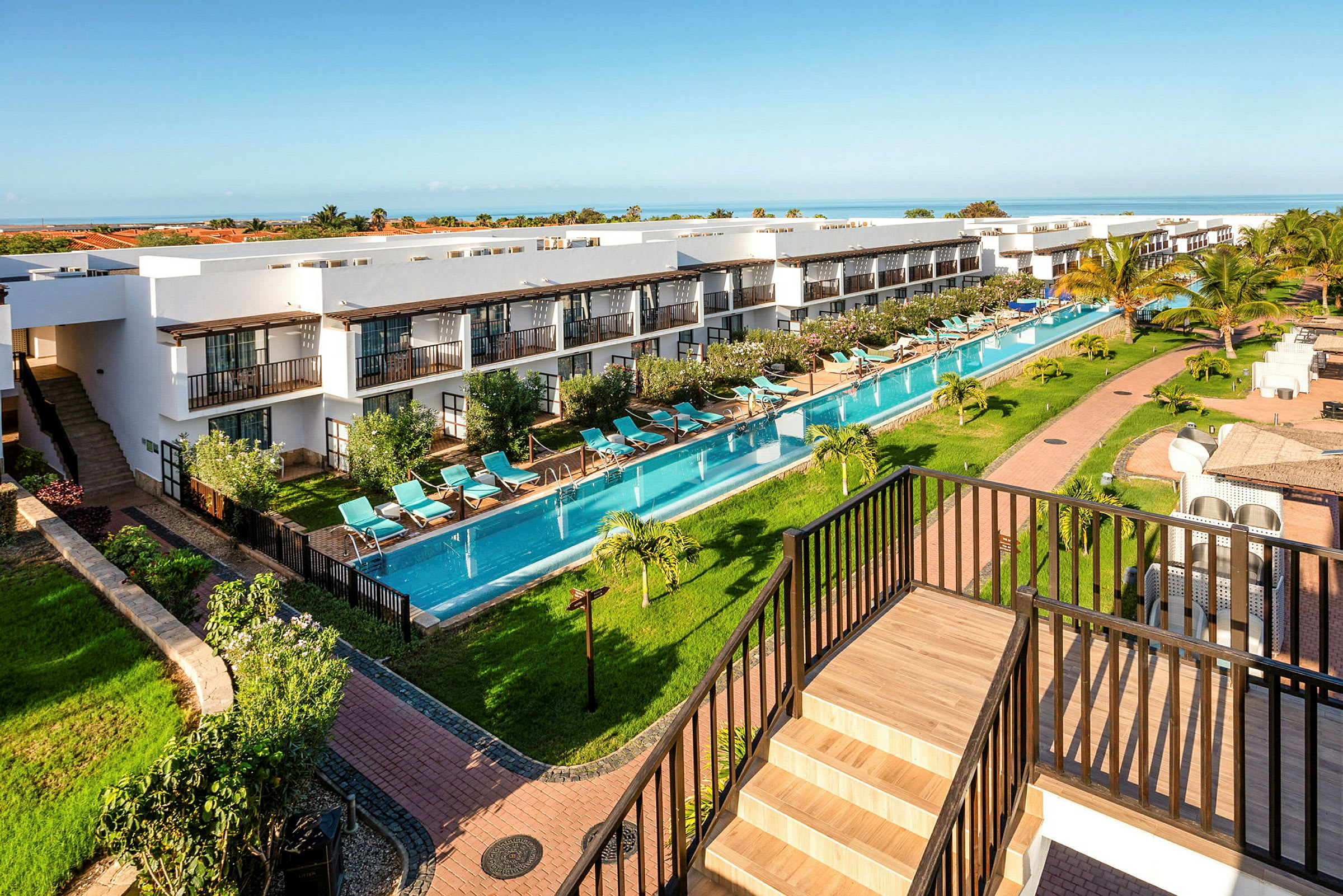 En oversigt over en resort med bygninger, en lang pool og frodige omgivelser. (AI-genereret tekst)