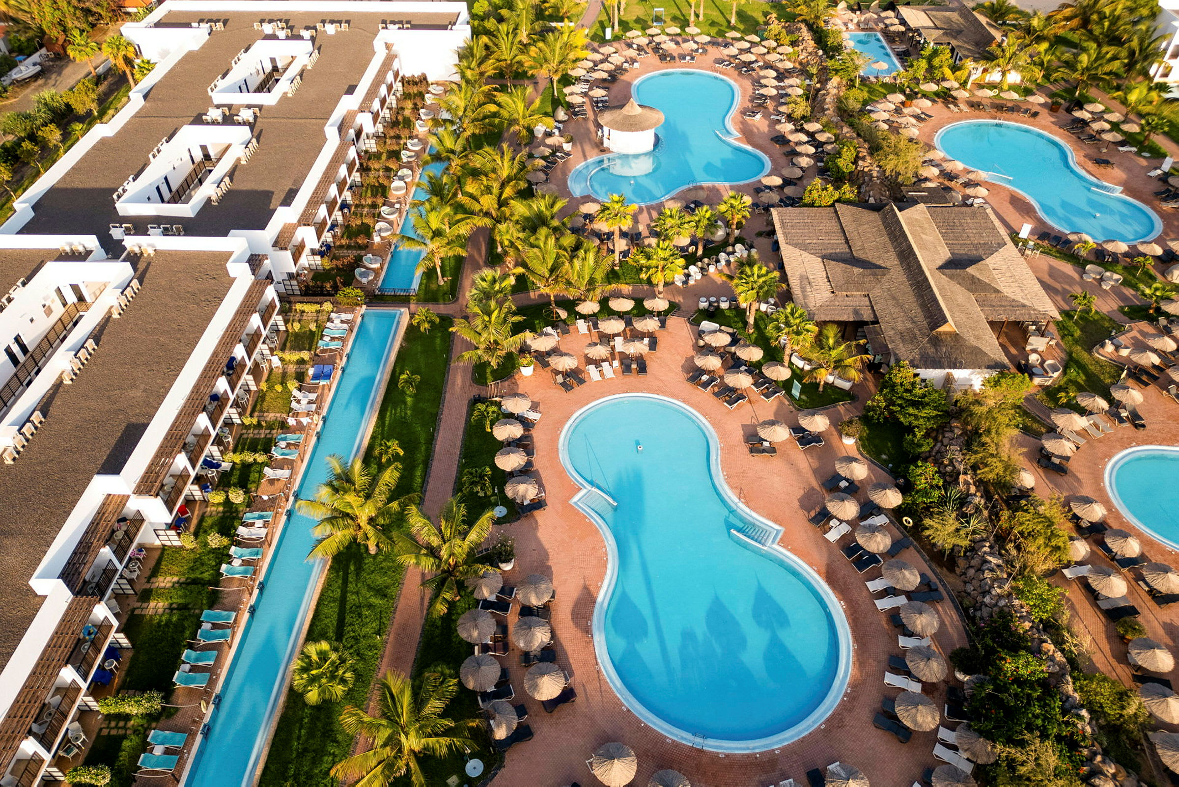 Luftfoto af hotelområde med pools, liggestole og grønt område. (AI-genereret tekst)