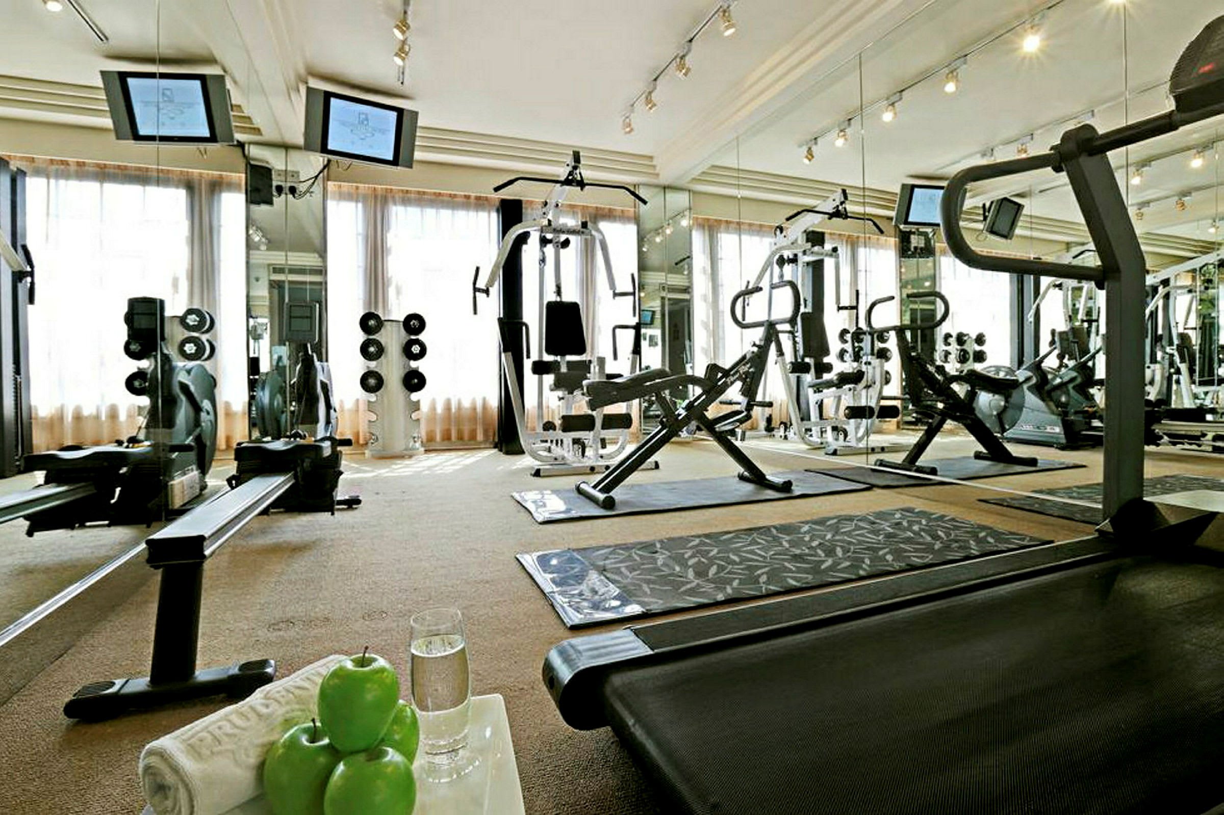 Et fitnesscenter med træningsmaskiner, vægte og spejle. På et bord ligger grønne æbler og et glas vand. (AI-genereret tekst)