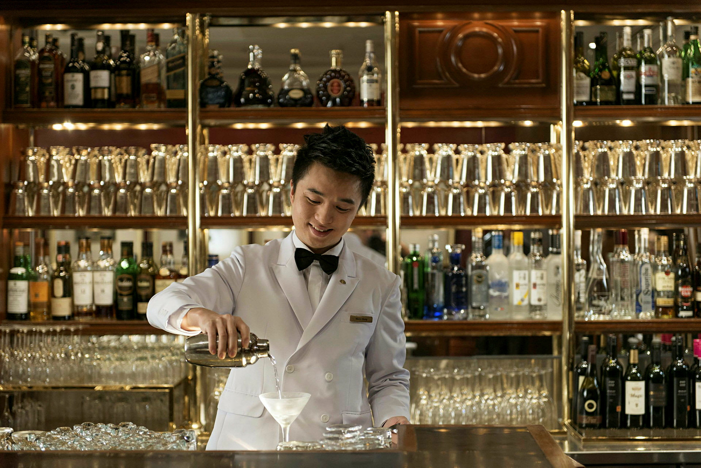 En bartender klædt i hvid jakke, der serverer en drink foran en veludstyret bar. (AI-genereret tekst)