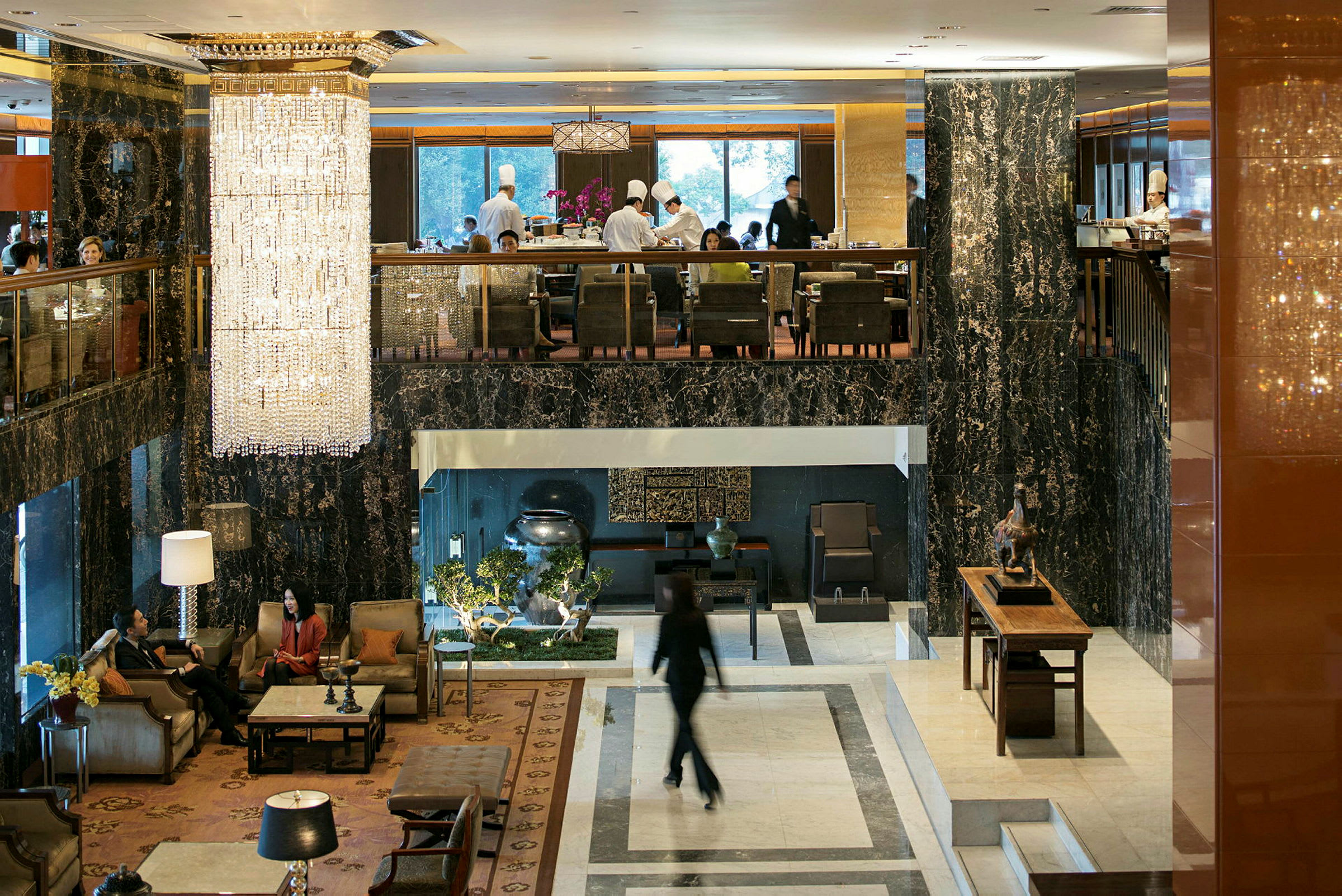 Hotellobby med elegante møbler, store vinduer og en stor lysekrone, der hænger fra loftet. (AI-genereret tekst)