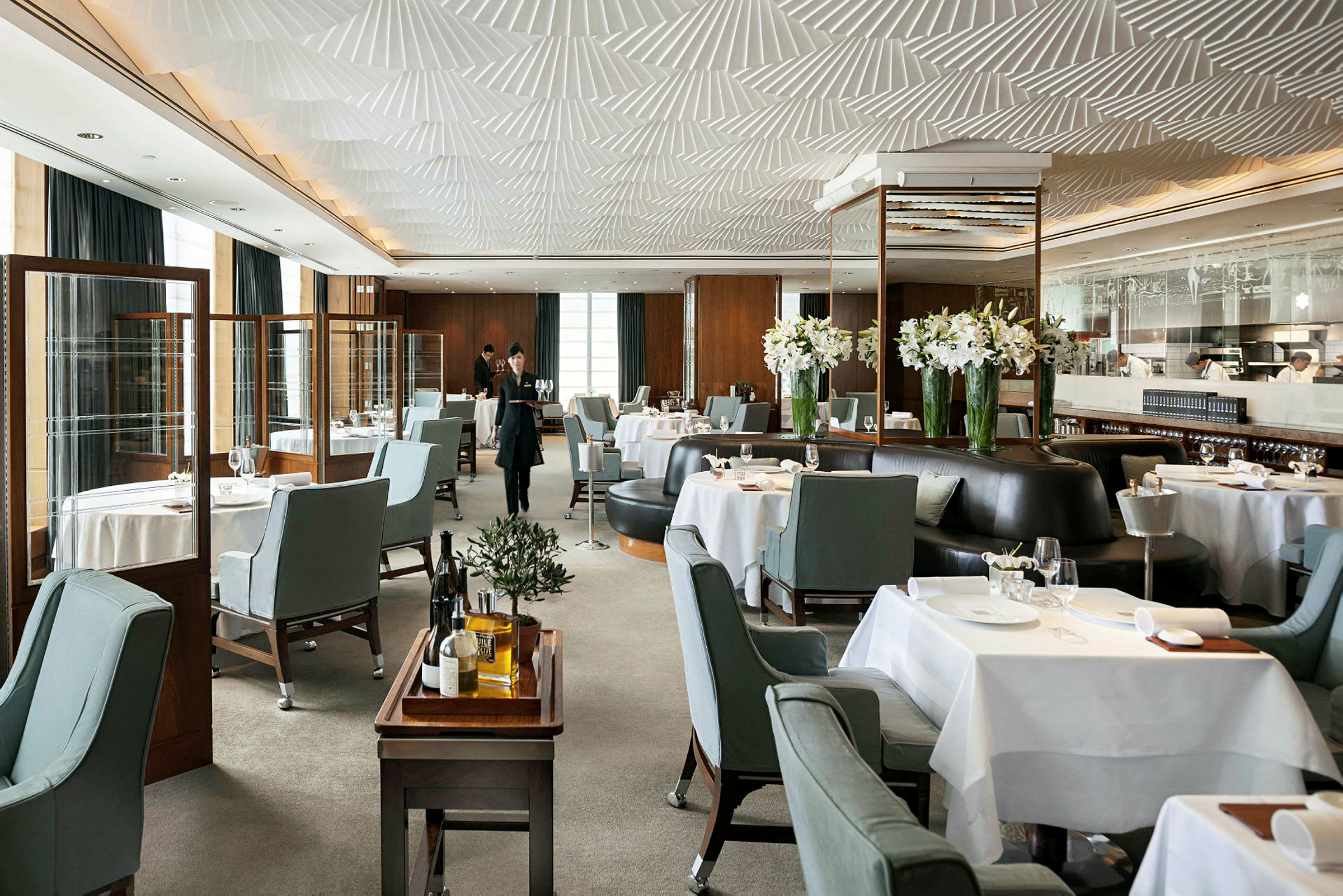 Det er en elegant restaurant med opdækkede borde, blågrå stole og dekorationer med hvide blomster. (AI-genereret tekst)