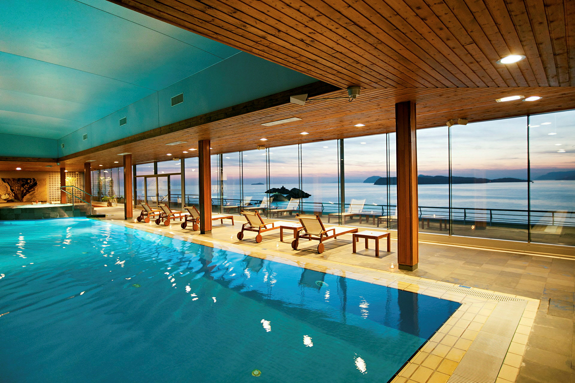 En indendørs pool i et spa med udsigt til havet gennem store panoramavinduer. (AI-genereret tekst)