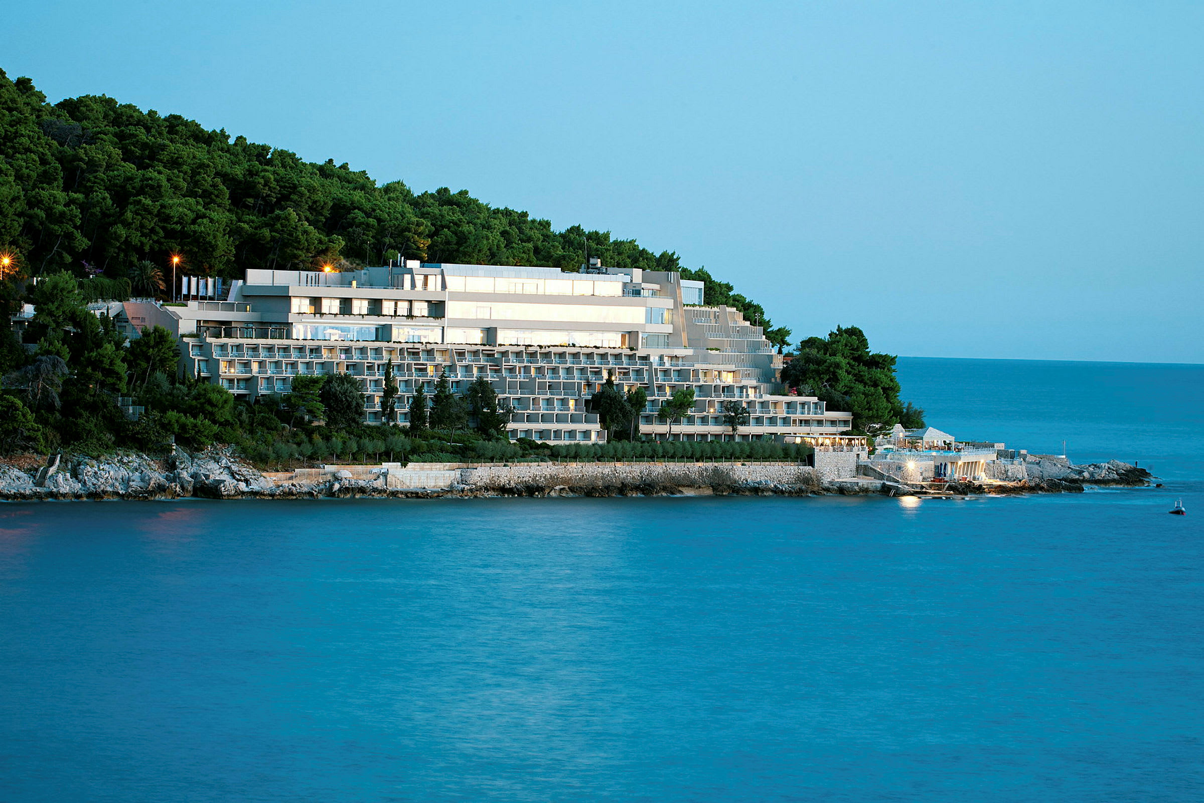 Et stort hotelkompleks beliggende ved havet, omgivet af frodig skov. (AI-genereret tekst)