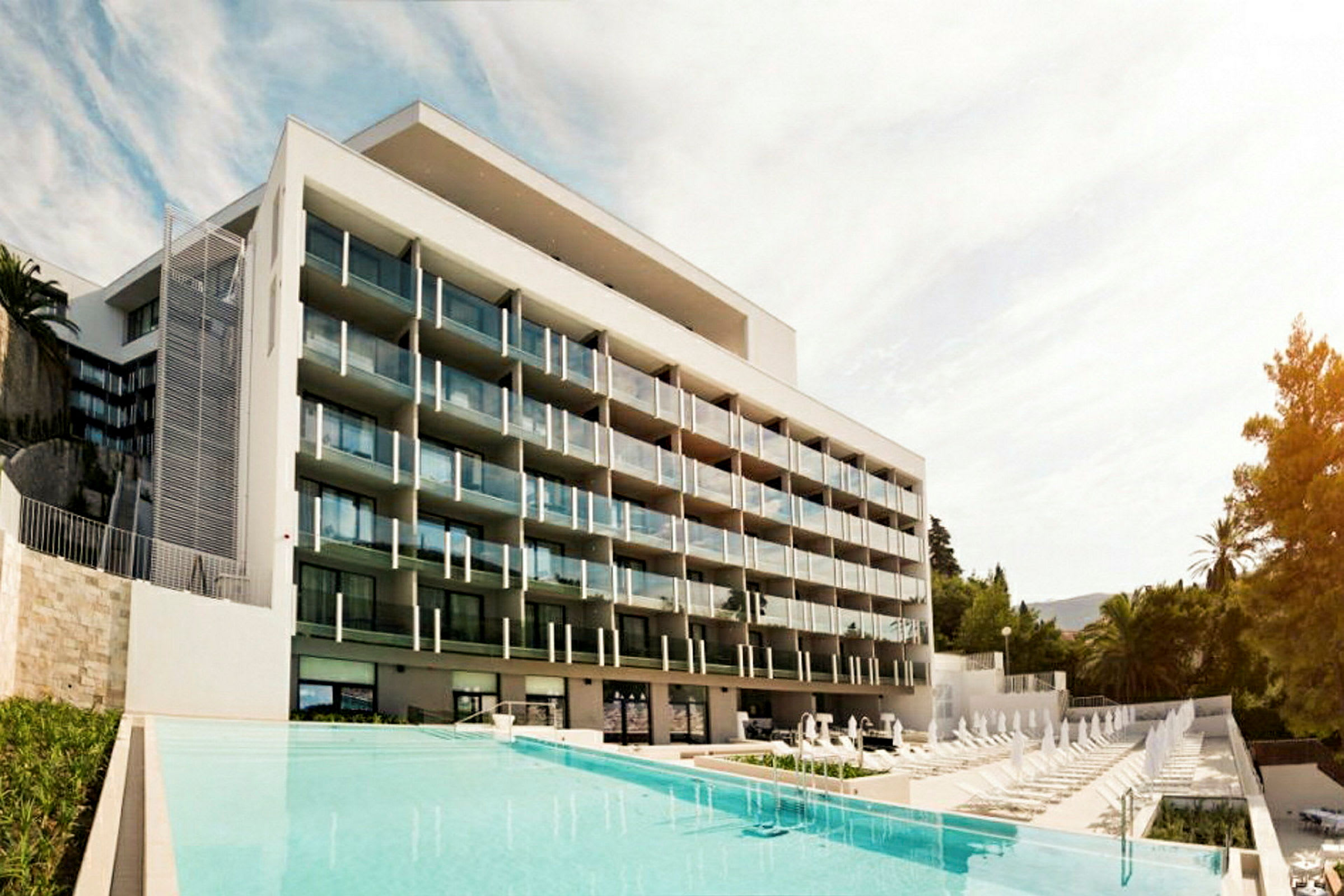 Et moderne hotel med flere altaner foran en pool. (AI-genereret tekst)