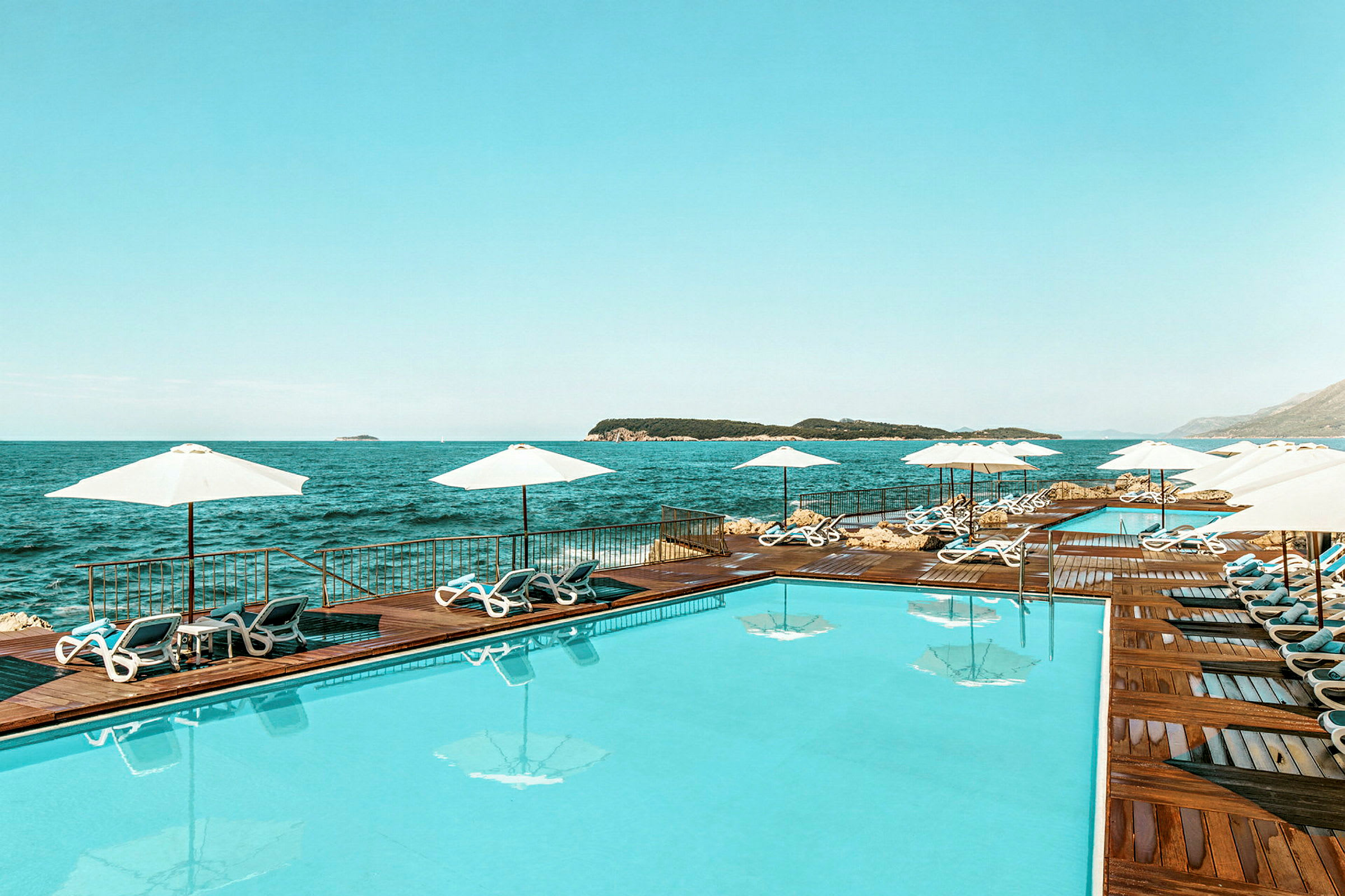 En swimmingpool ved havet, omgivet af solsenge og parasoller. (AI-genereret tekst)