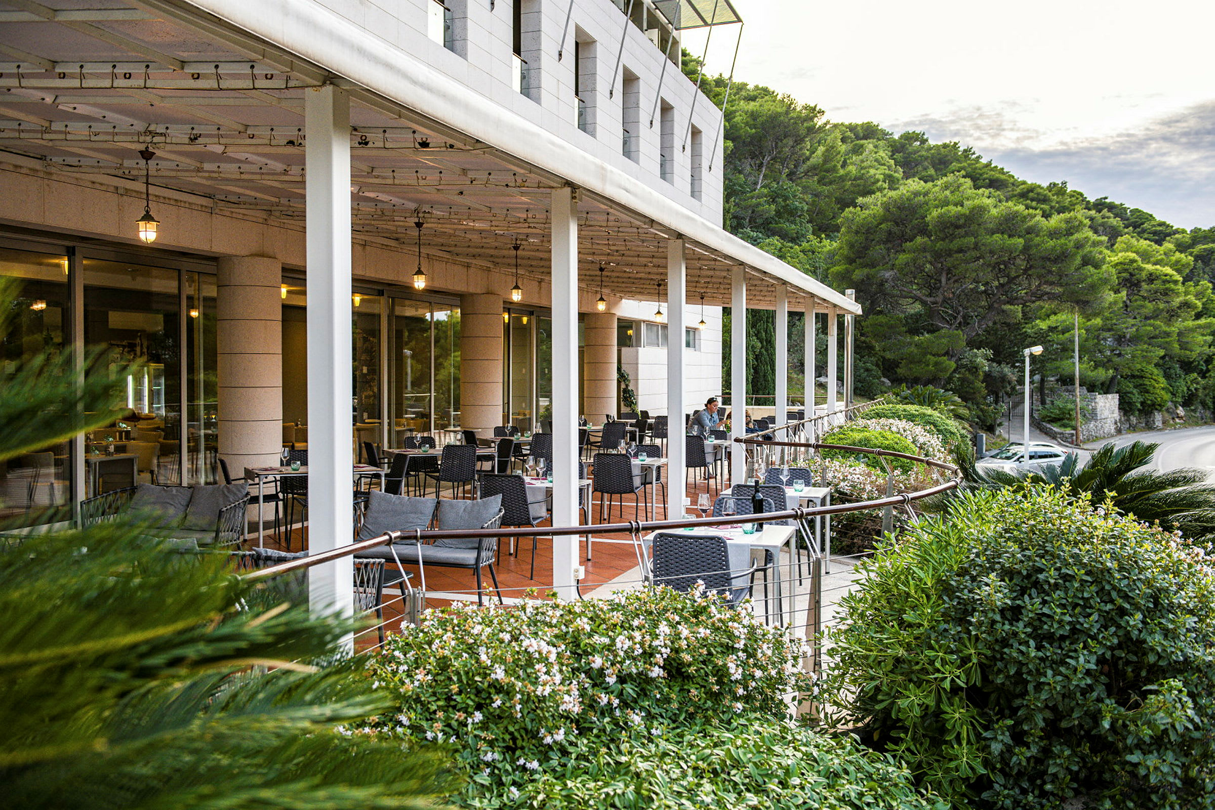 Restaurantterrasse med borde og stole omgivet af grønne omgivelser. (AI-genereret tekst)