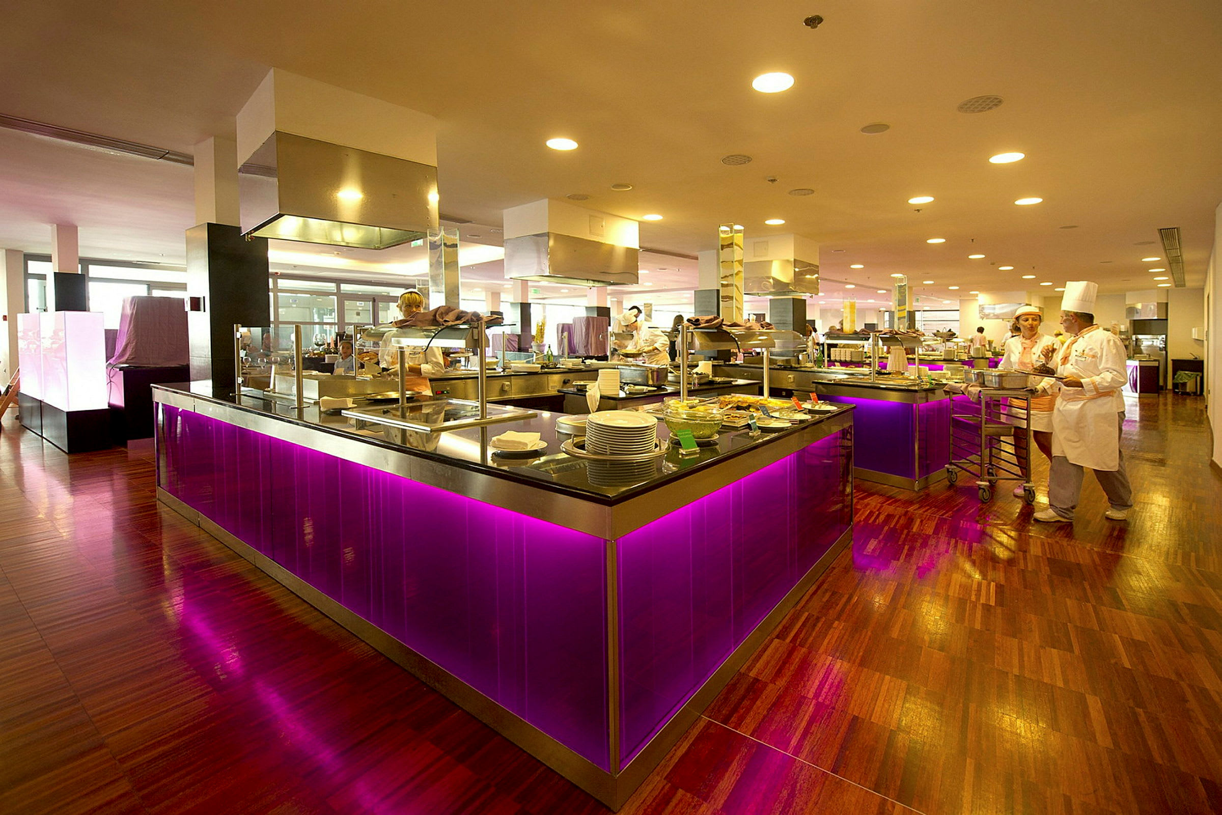 Billede af en restaurant eller buffetområde med moderne og farverige interiørdetaljer, inklusive lysende lilla belysning under diske. (AI-genereret tekst)