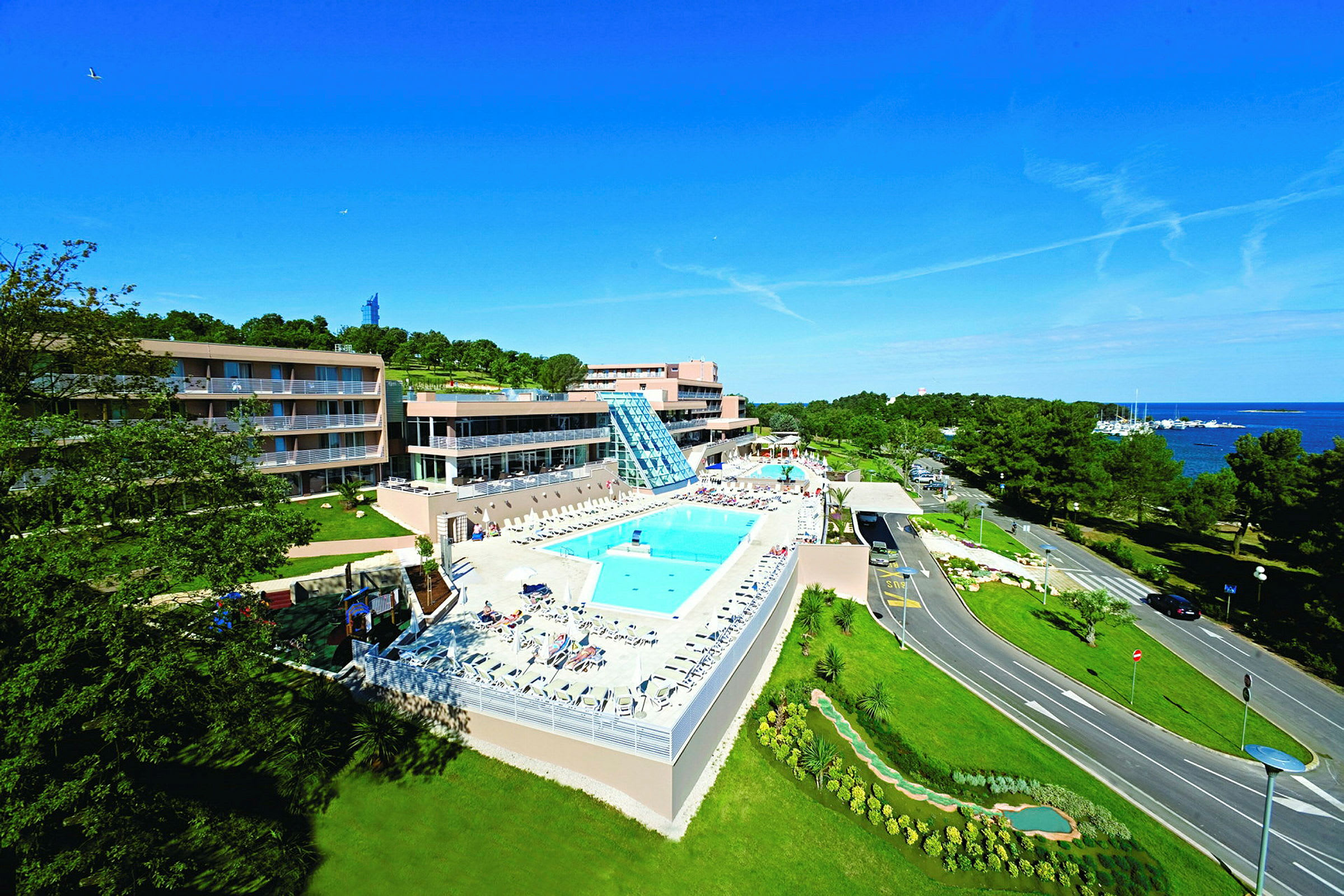 Billede af et hotelkompleks med pool og grønne omgivelser nær havet. (AI-genereret tekst)
