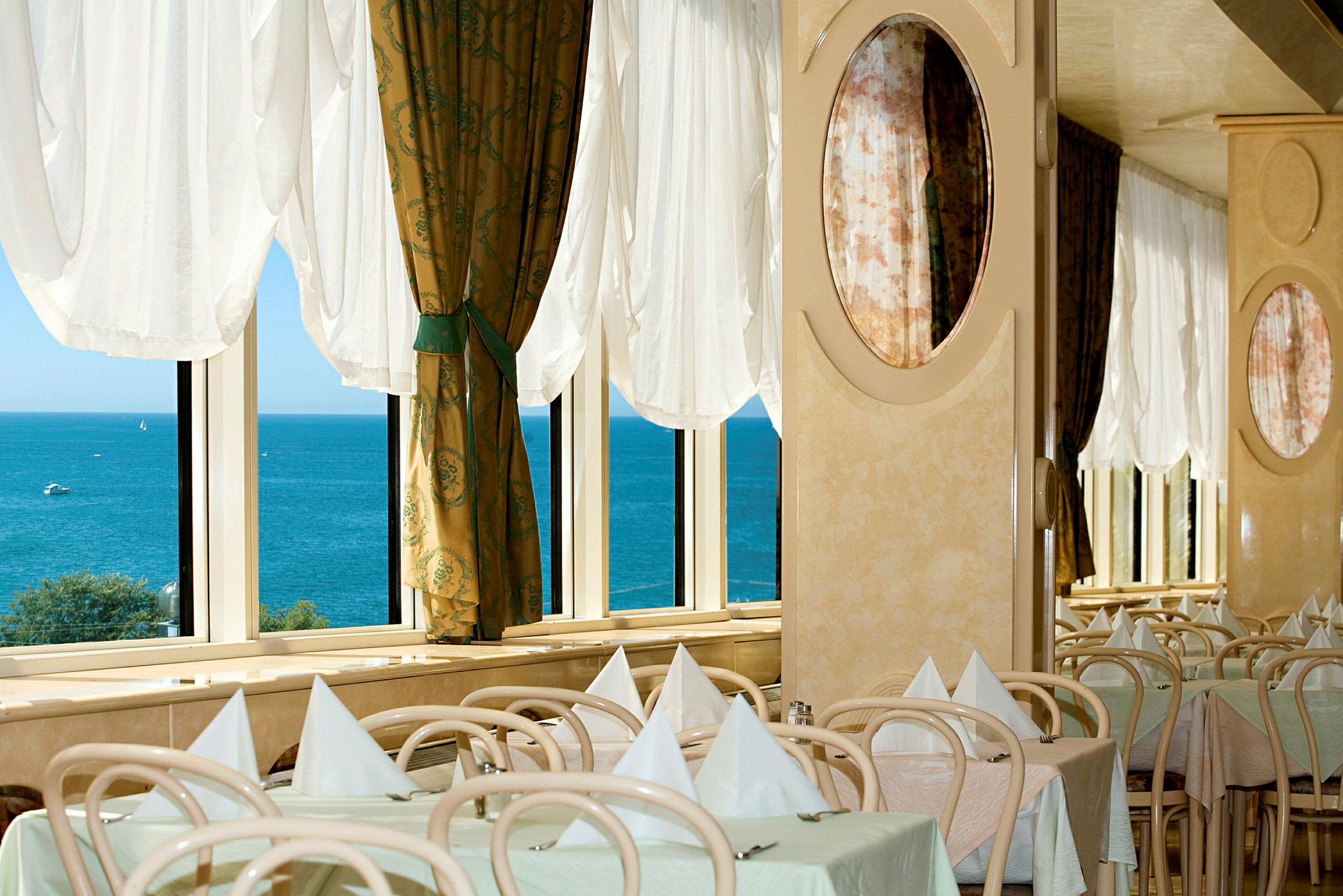 Restaurant med dækkede borde ved vinduer med udsigt over havet. (AI-genereret tekst)