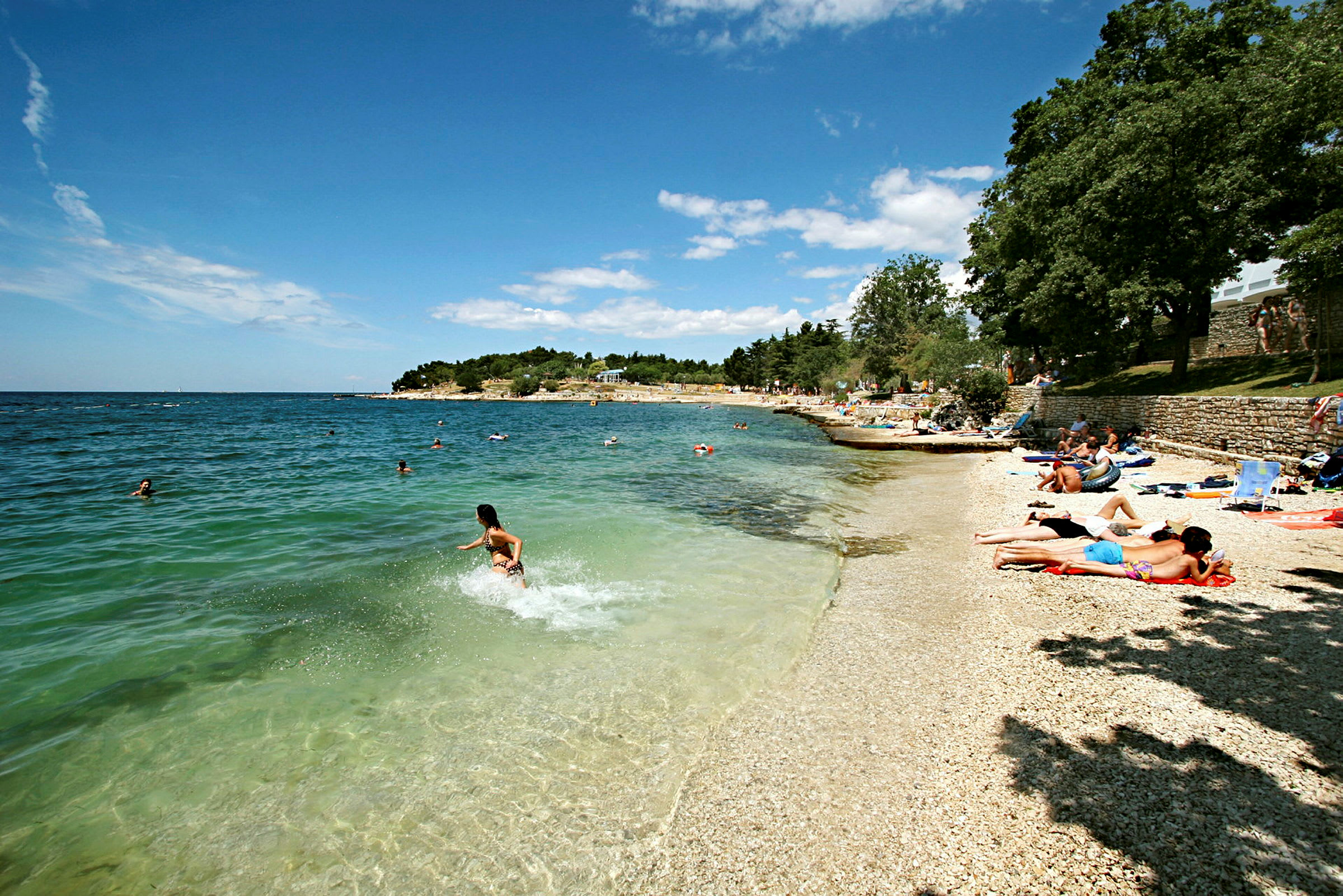 En strand med småsten, hvor folk soler sig og bader i det klare blå hav. (AI-genereret tekst)