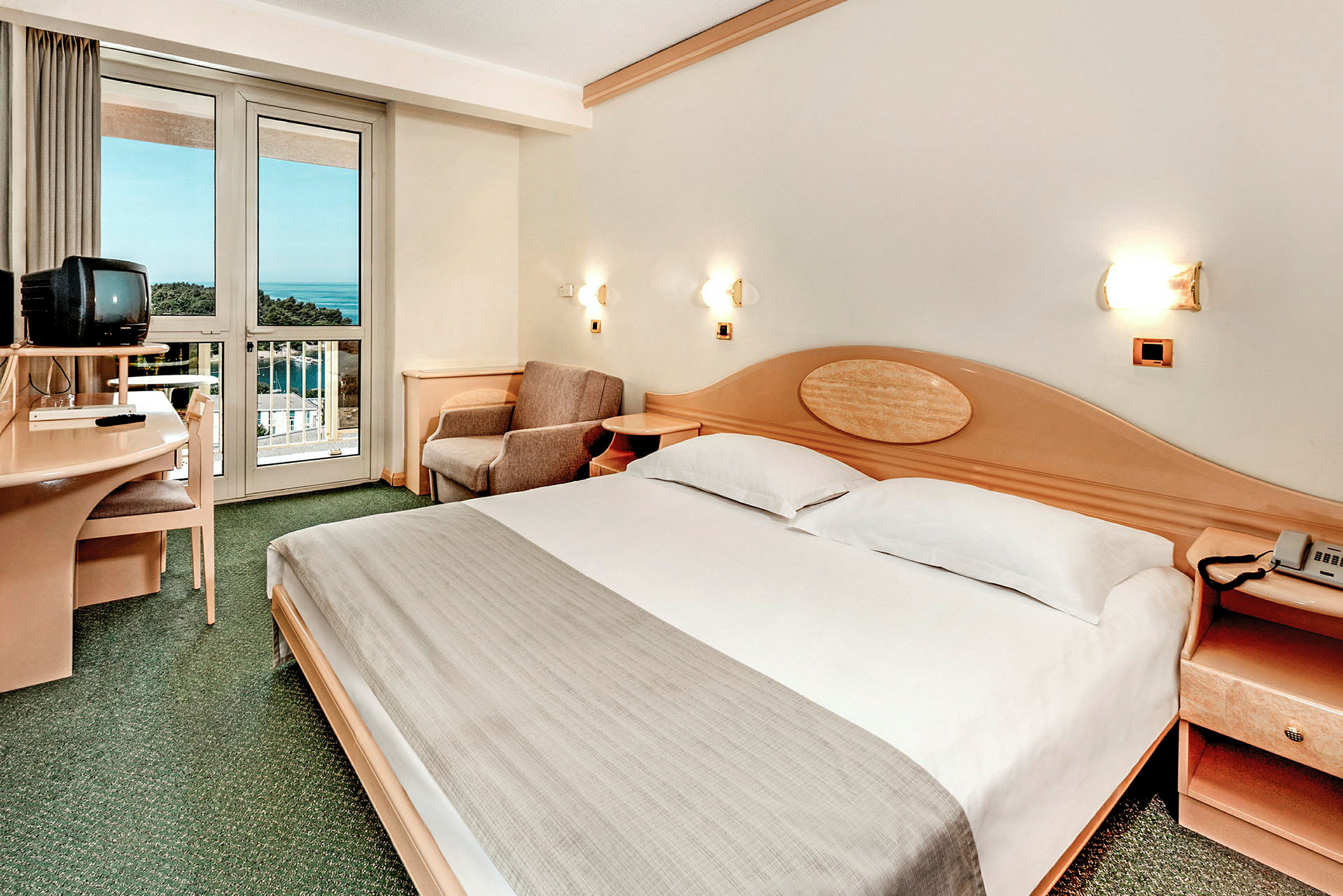 Et hotelværelse med en dobbeltseng, et fjernsyn på et skrivebord og en balkon med udsigt over havet. (AI-genereret tekst)