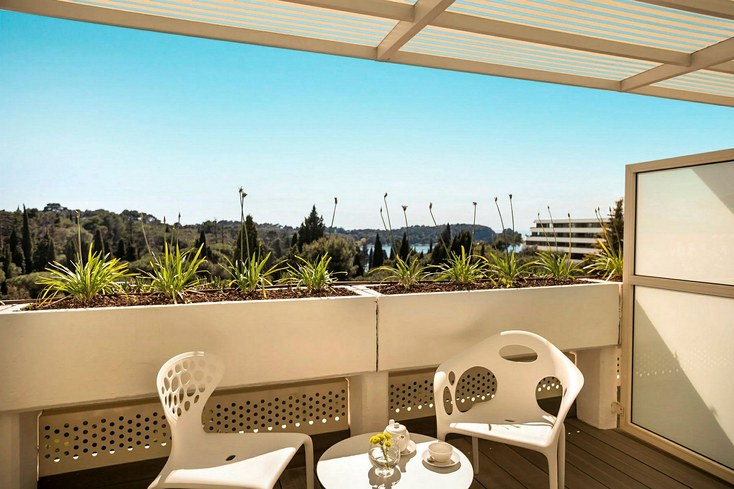 Terrasse med to moderne hvide stole og et rundt bord, udsigt over grønt område og blå himmel. (AI-genereret tekst)