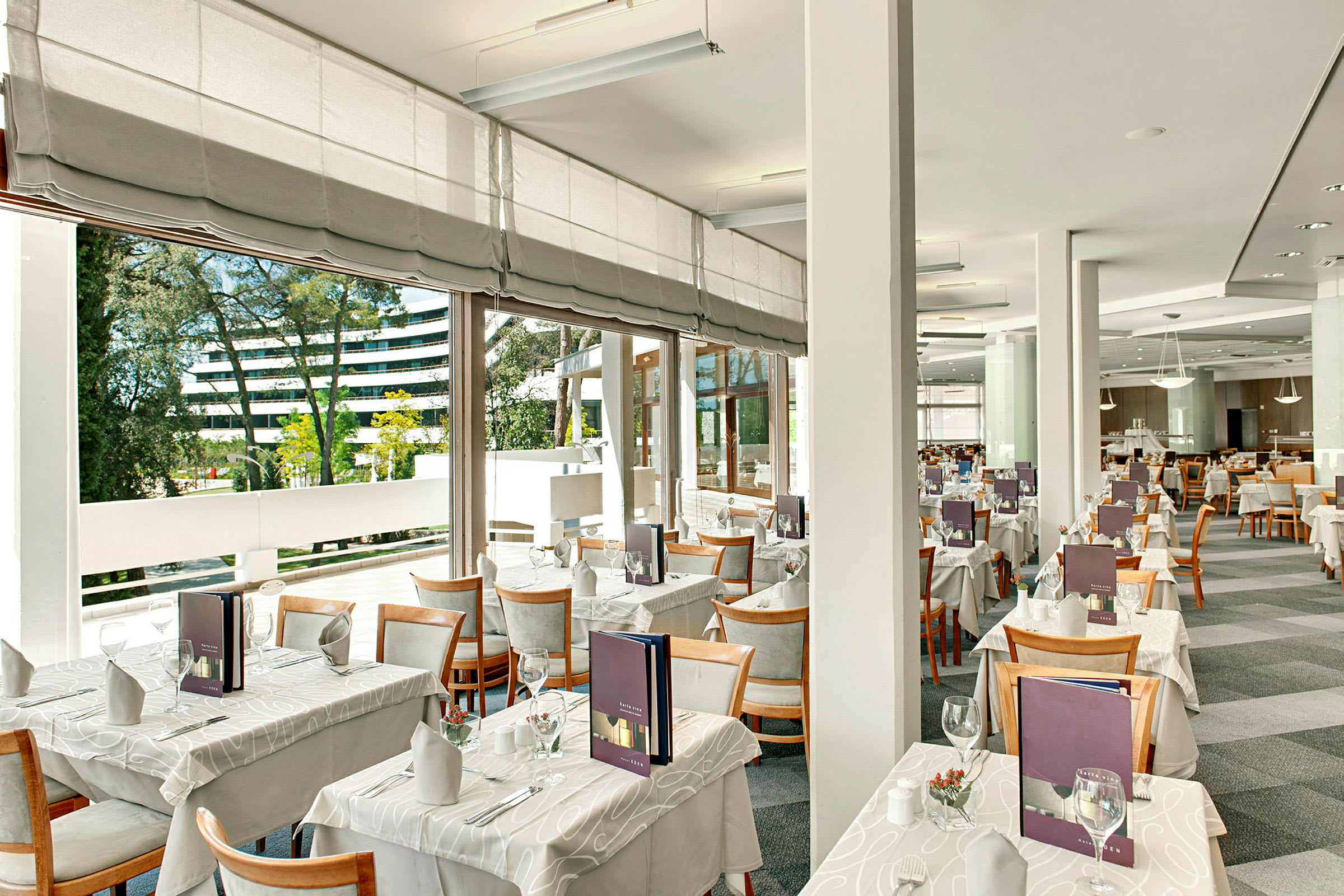 Moderne og lyst restaurantområde med dækkede borde og store vinduer. (AI-genereret tekst)