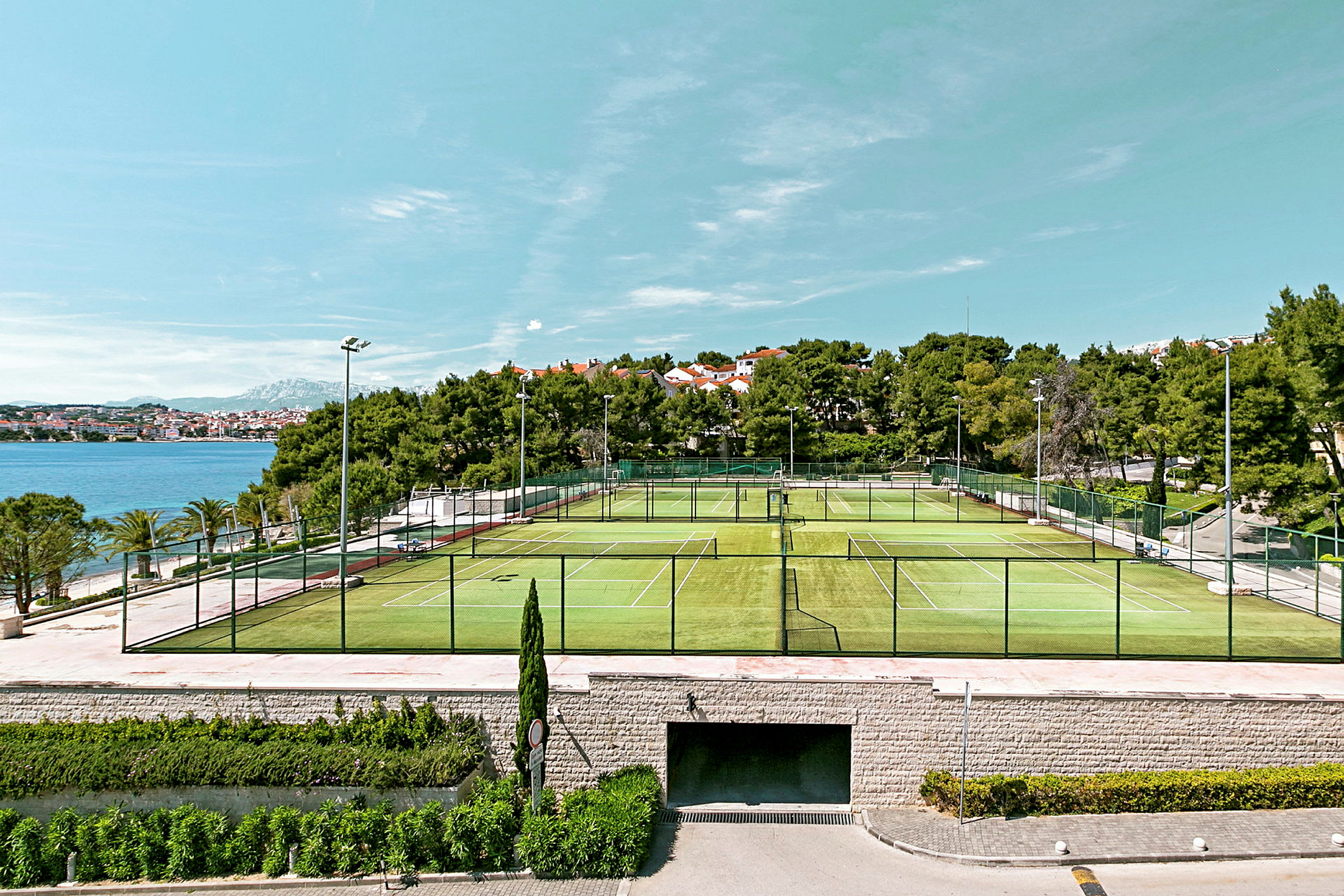 Billede af udendørs tennisbaner med havet og bygninger i baggrunden. (AI-genereret tekst)