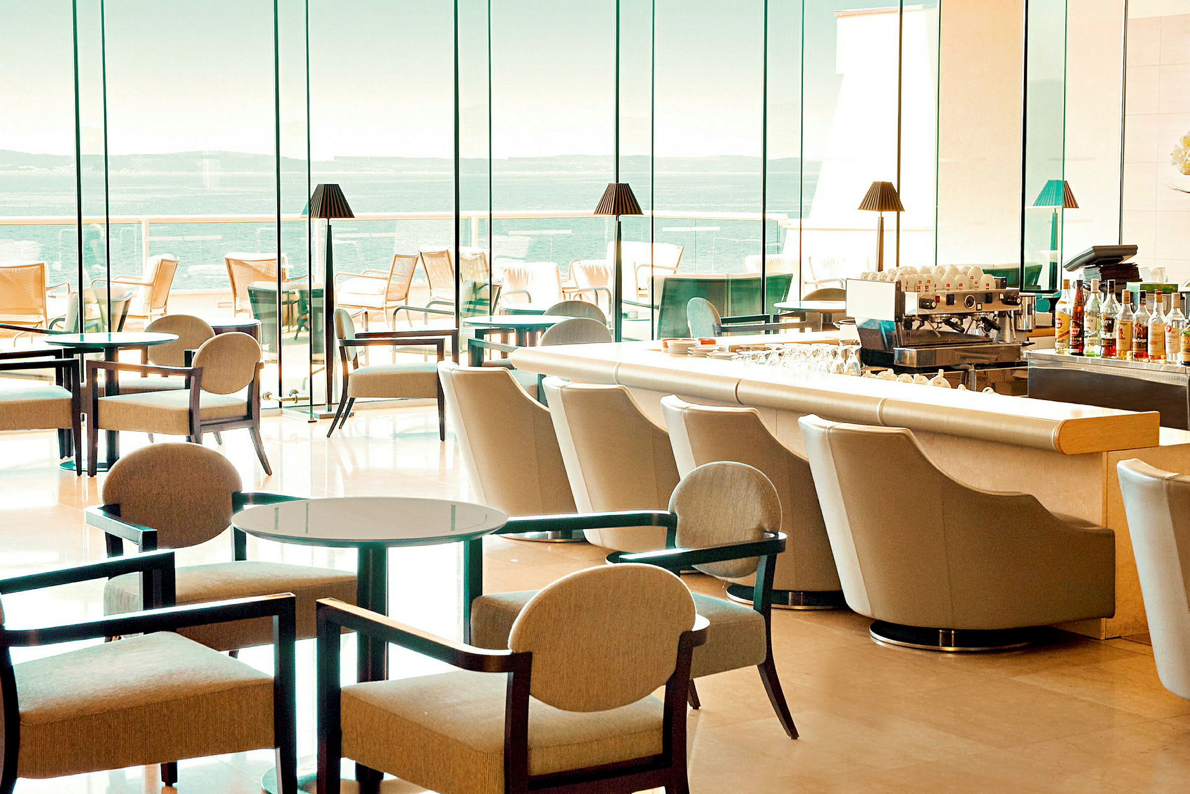 Hotelbar med moderne møbler og store glasvinduer med udsigt over havet. (AI-genereret tekst)