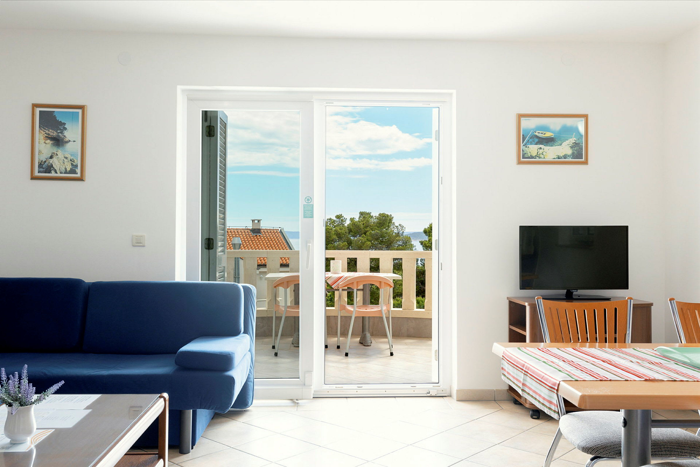 Stue med blå sofa og spisebord ved siden af en balkon med havudsigt. (AI-genereret tekst)