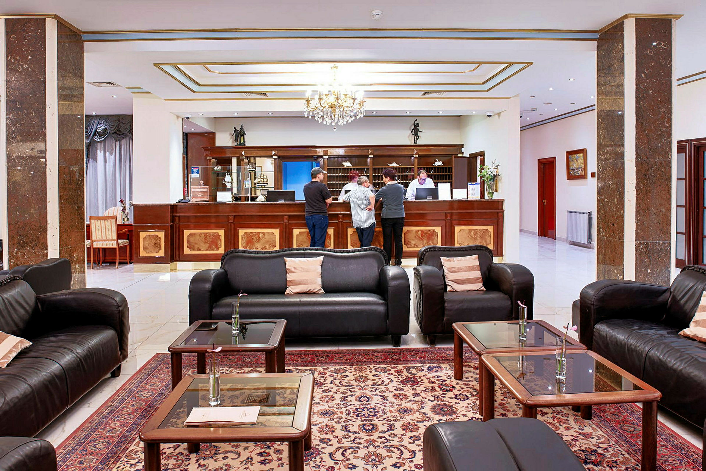 Hotellobby med sofaer, sofaborde og receptionsskranke hvor flere personer står. (AI-genereret tekst)