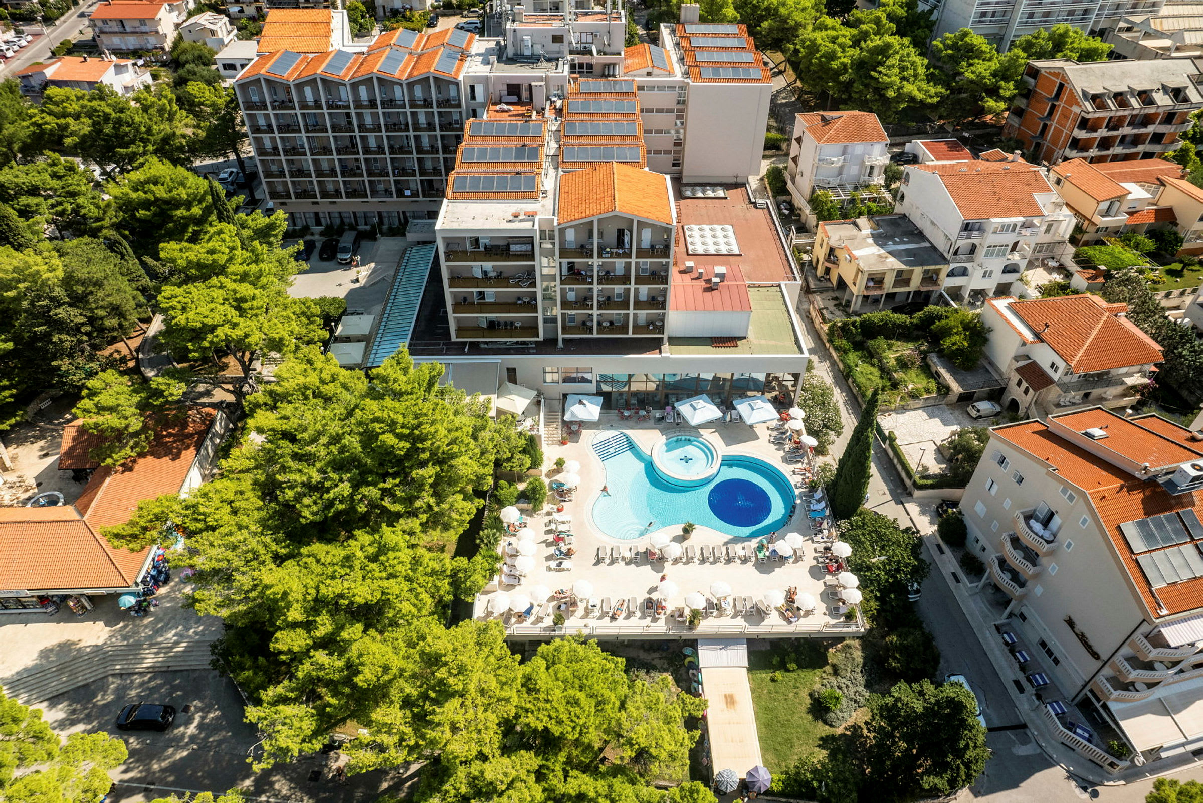 Luftfoto af hotel med poolområde og omkringliggende bygninger. (AI-genereret tekst)