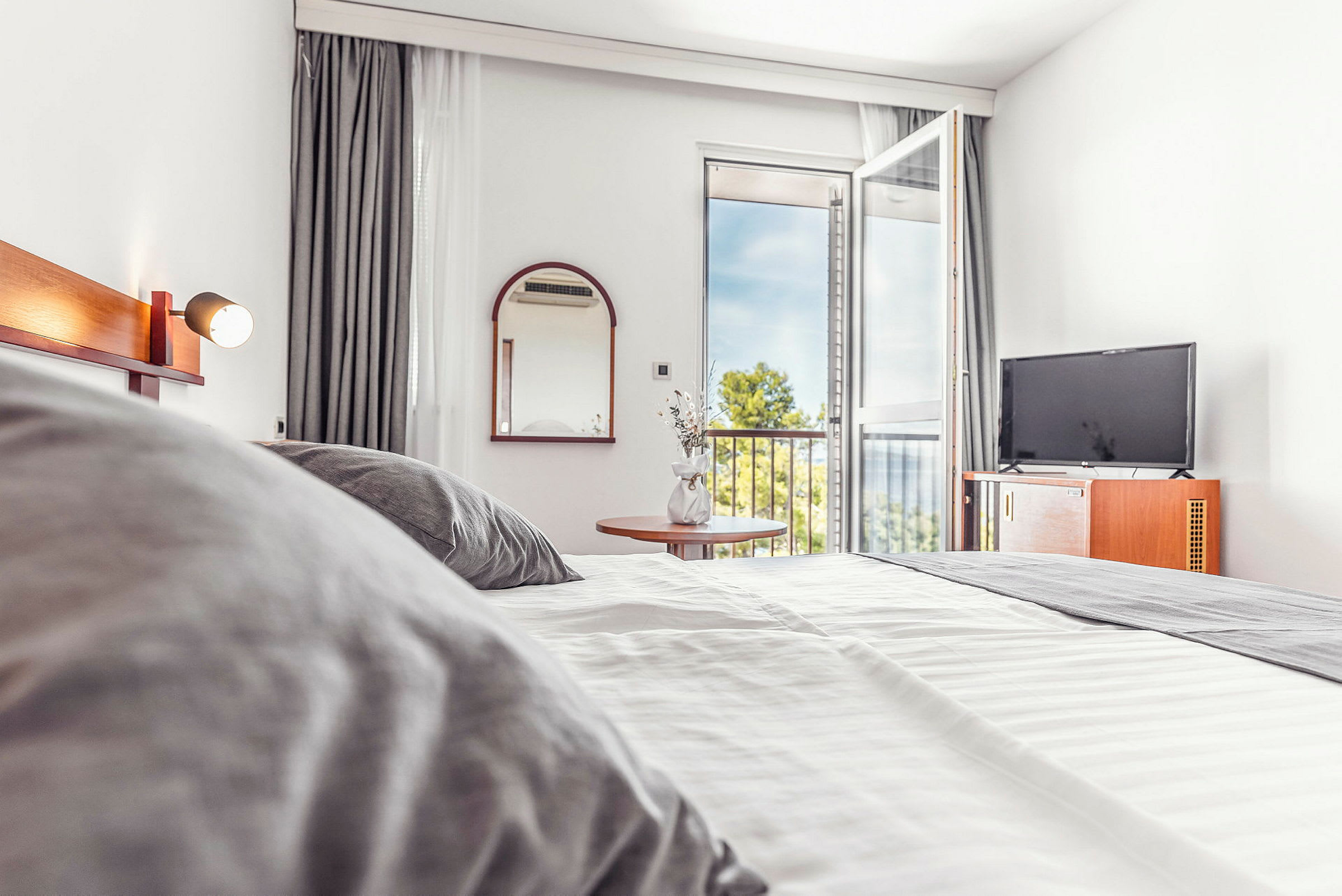 Hotelværelse med seng, TV og åben altandør. (AI-genereret tekst)