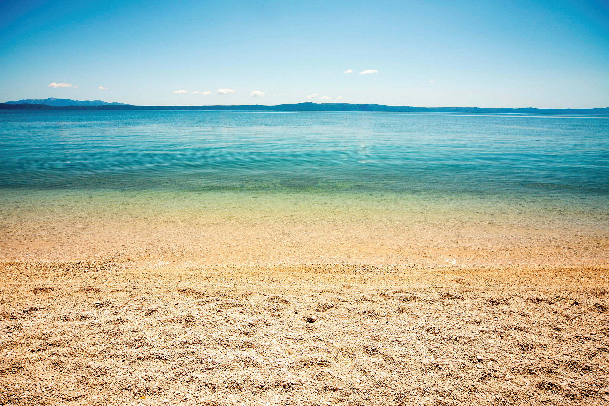 En strand med småsten ved klart vand og en fjern horisont. (AI-genereret tekst)