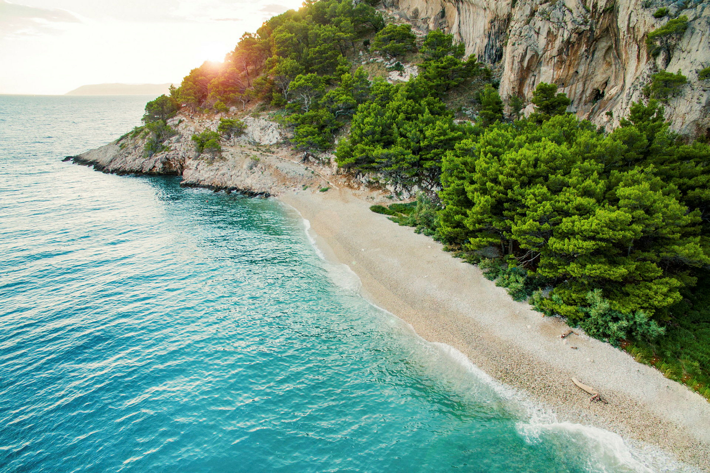 En afsides strand med grønne træer og klipper ved kanten af havet. (AI-genereret tekst)