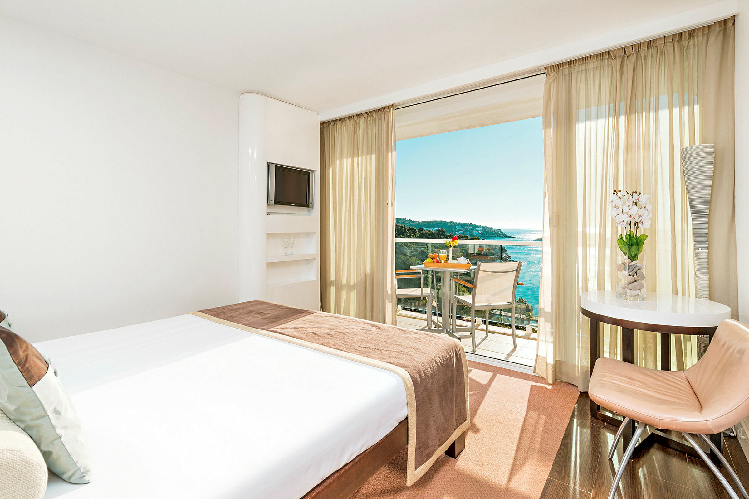 Hotelværelse med en stor seng, der vender ud mod en balkon med udsigt over havet. (AI-genereret tekst)