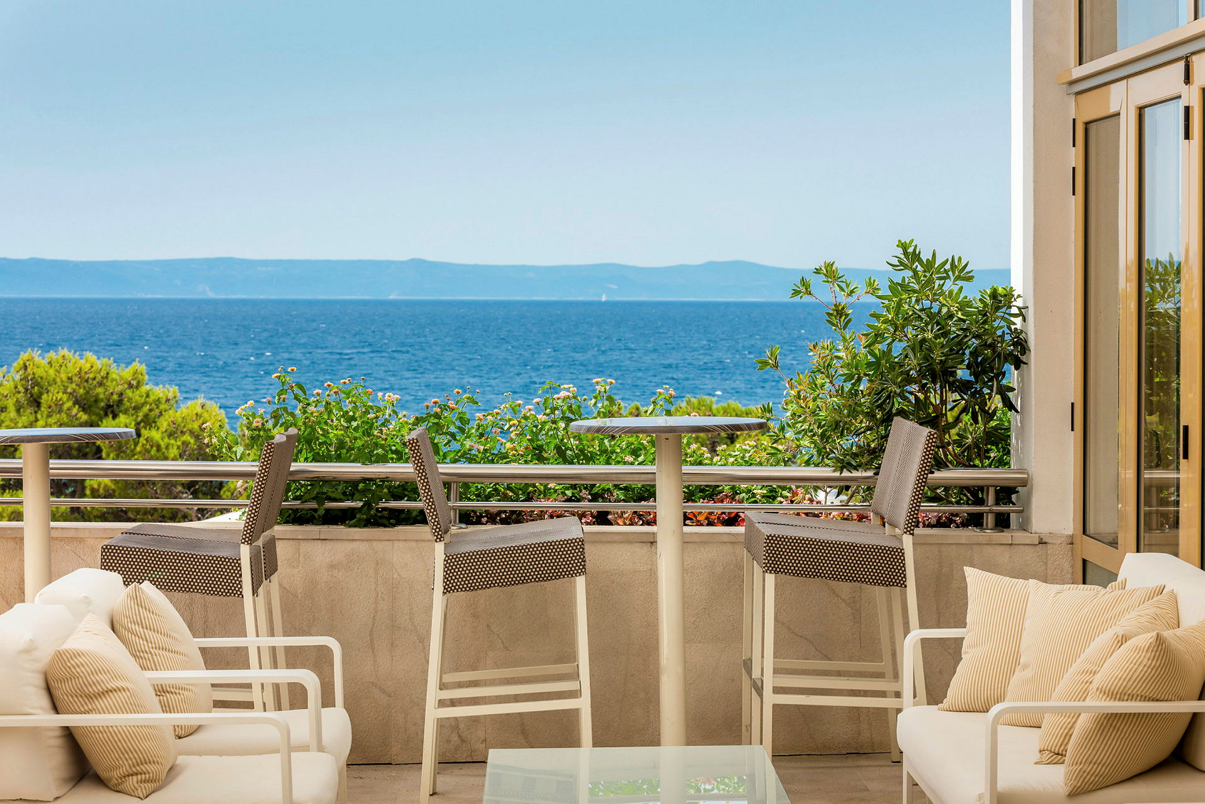 Udsigt fra en terrasse med siddepladser mod havet. (AI-genereret tekst)
